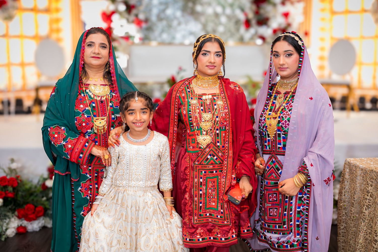 Group photo of wedding party members in vibrant traditional South Asian outfits with floral backdrop.