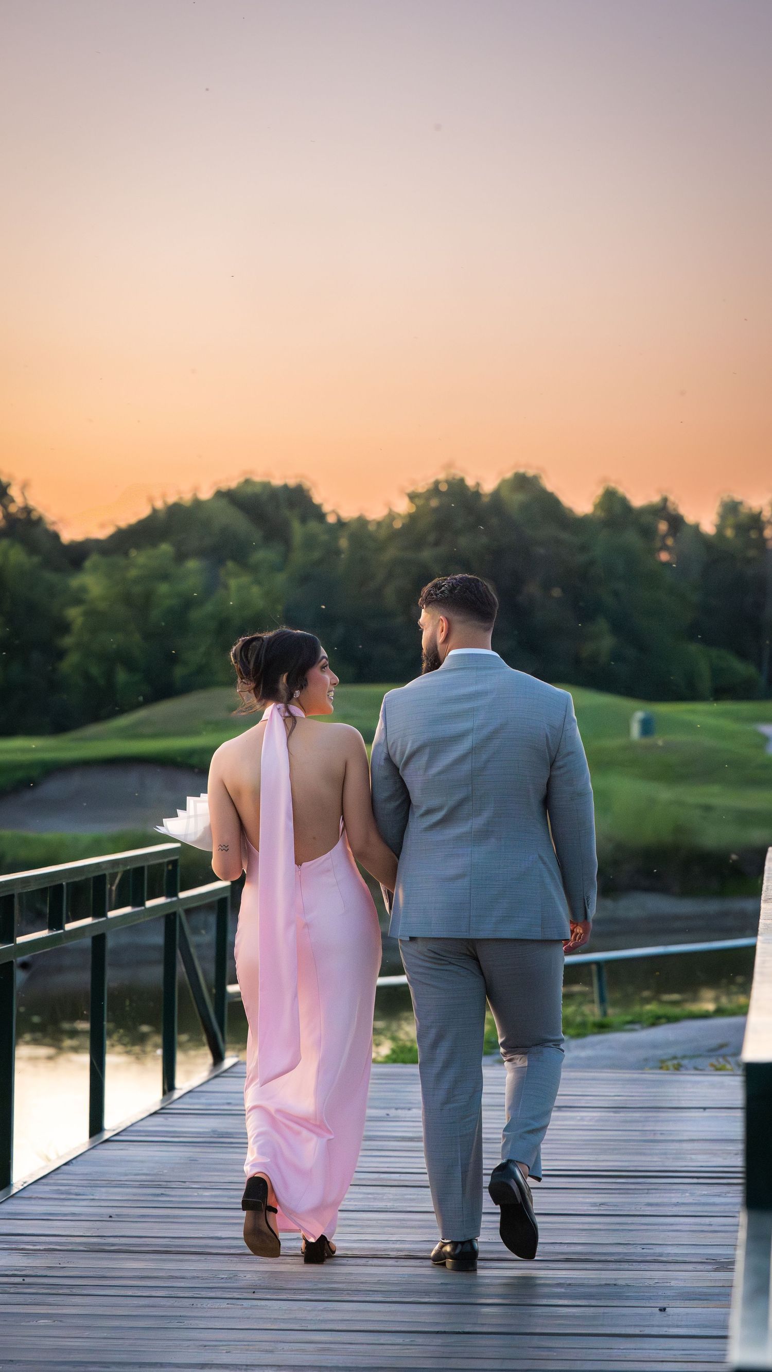 A couple walking away on a wooden boardwalk overlooking a scenic lake at sunset.