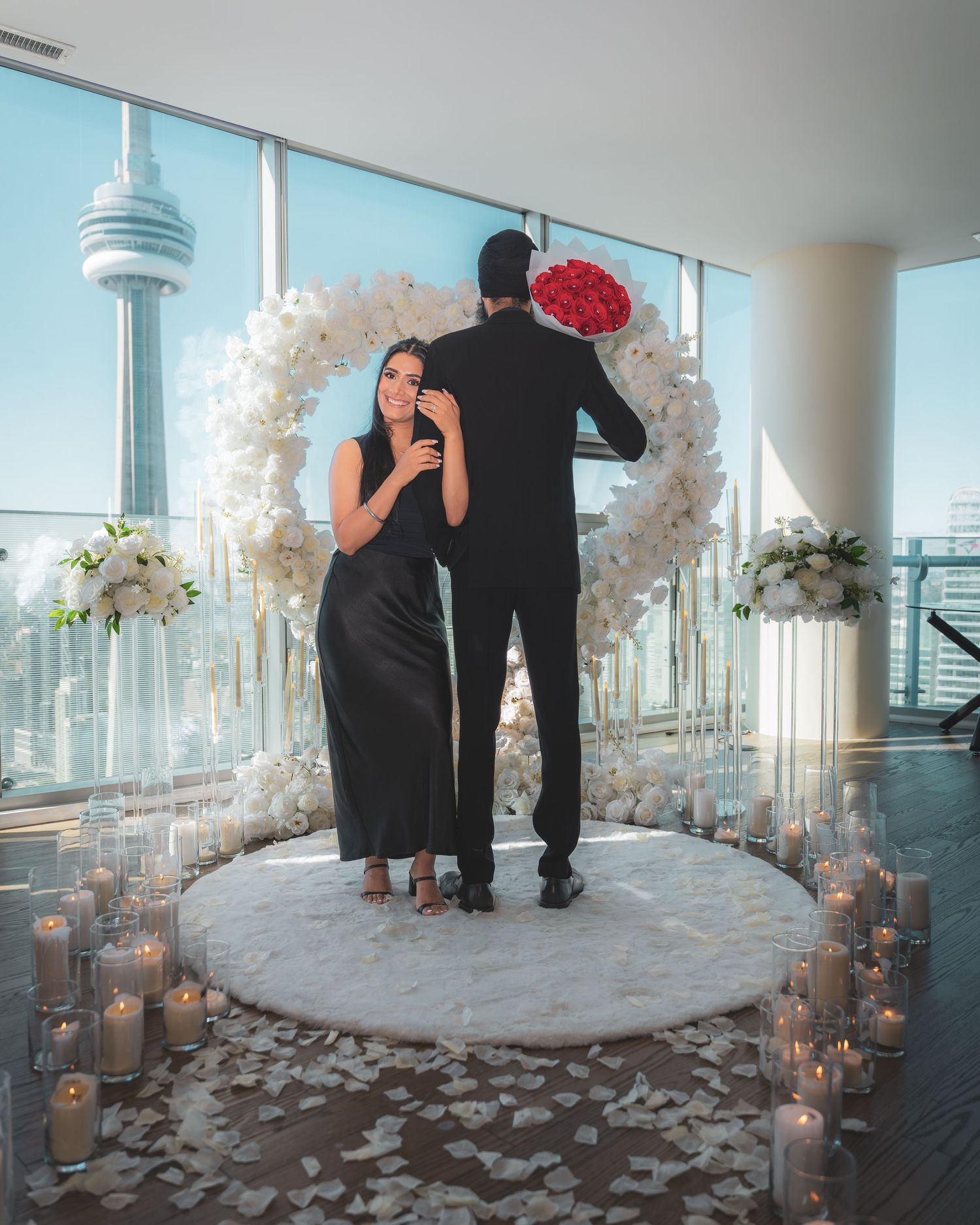 Romantic proposal setup in a high-rise venue with white floral arches, candles, and the CN Tower visible in the background.