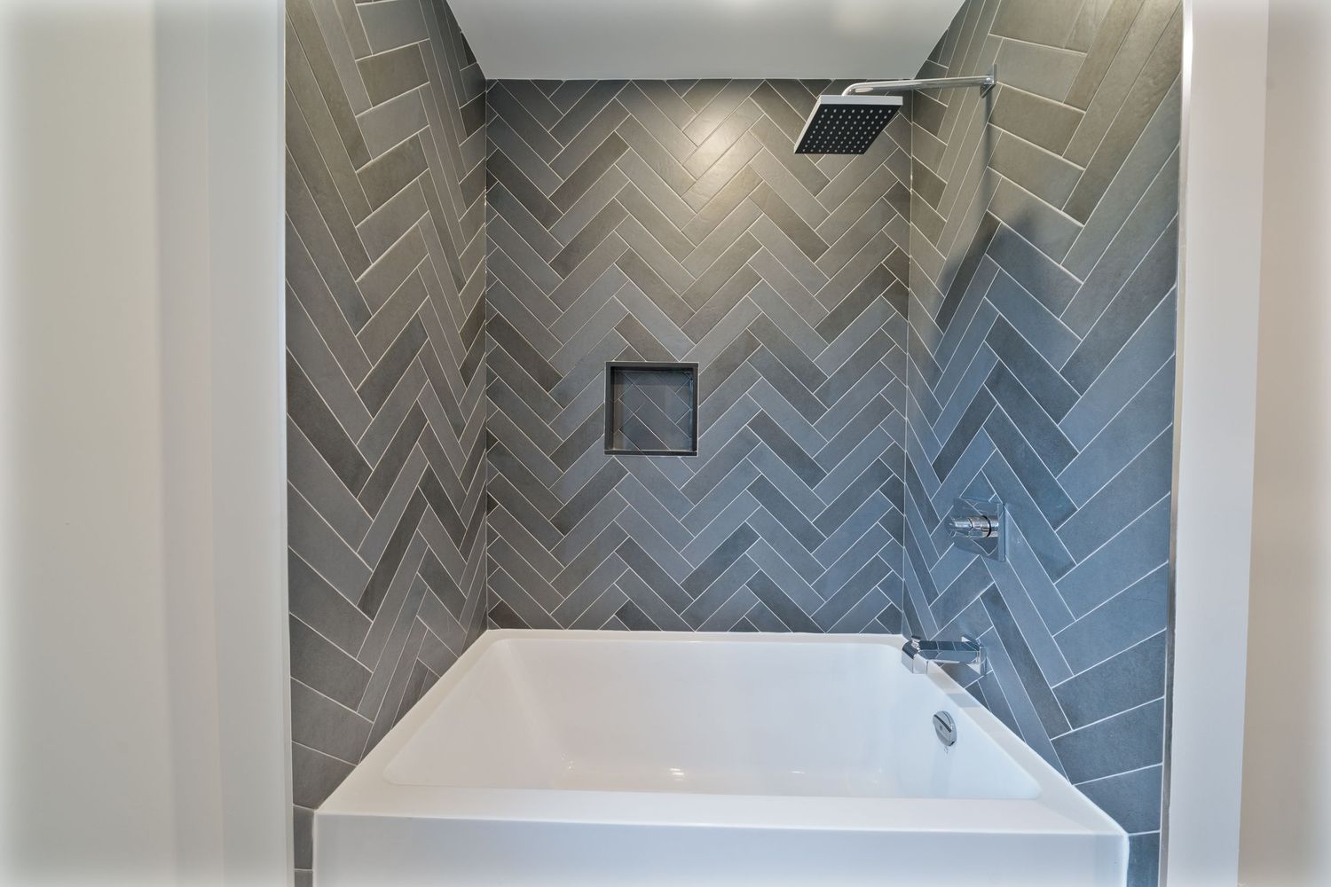 Contemporary bathroom with herringbone pattern grey tile walls and sleek white fixtures.
