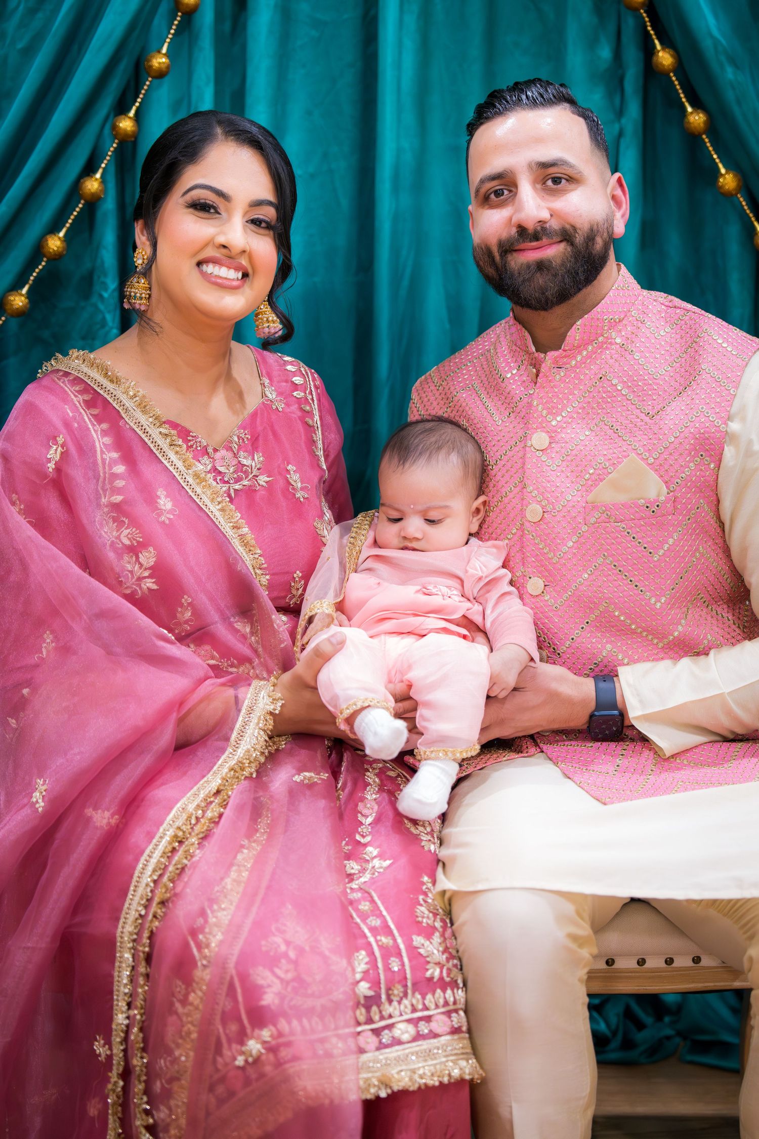South Asian family in pink traditional attire poses with newborn baby at cultural celebration.