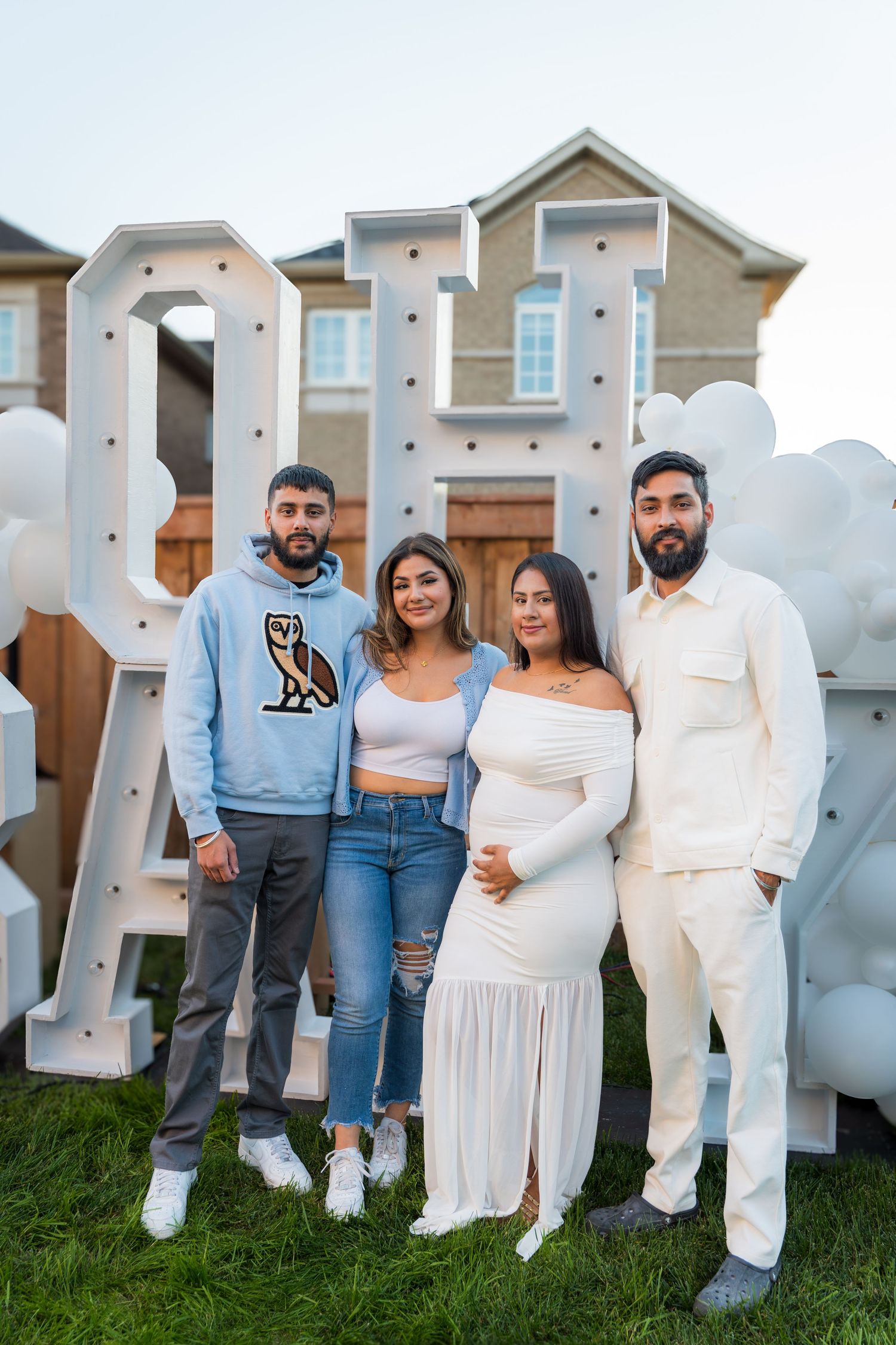 Group of four adults posing in front of OH BABY marquee letter display at a backyard gender reveal event.