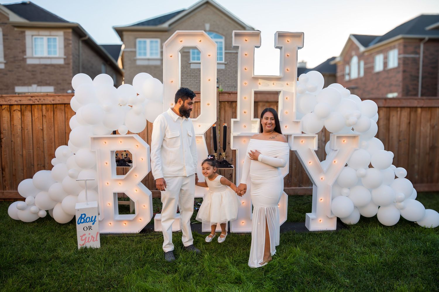 Family of three posing in front of OH BABY balloon letter display at outdoor baby shower.