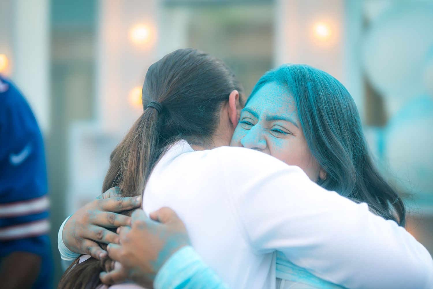 Two women share a warm embrace at an outdoor gender reveal party with blue powder.