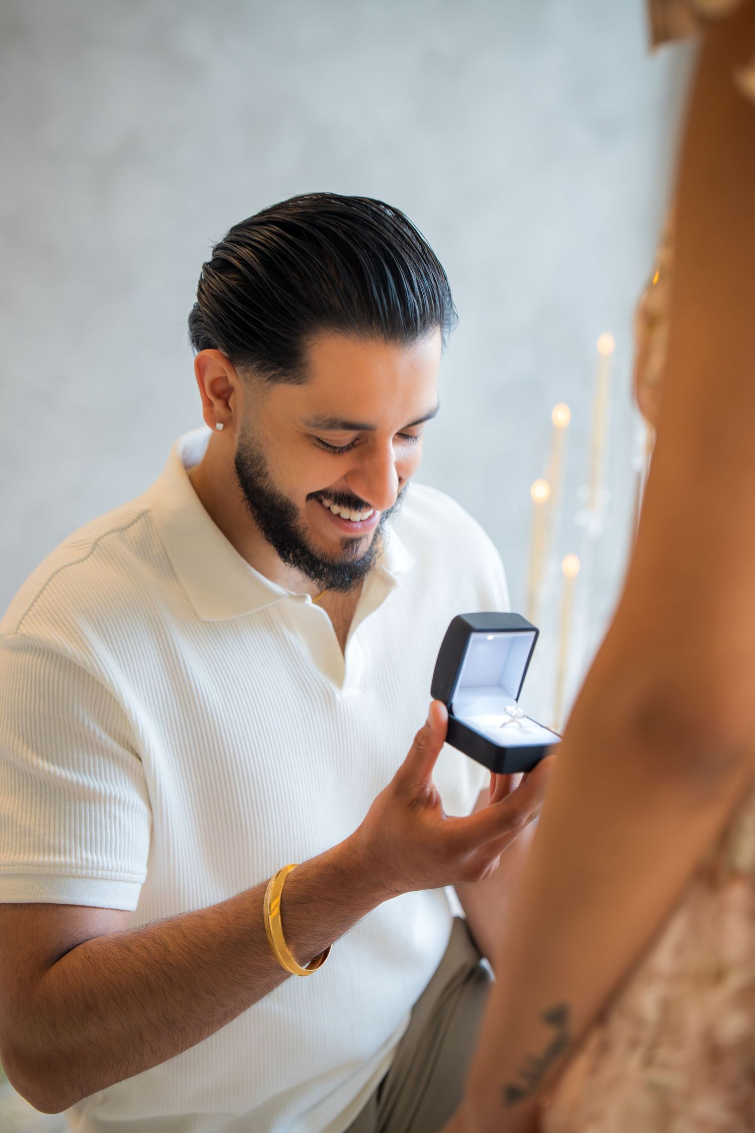 Smiling bearded man on one knee holding open ring box during a romantic marriage proposal.