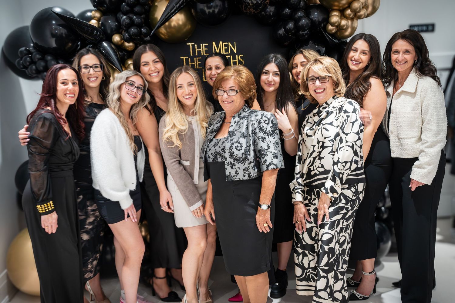 Celebratory gathering with guests posing against a backdrop of black and gold balloons.