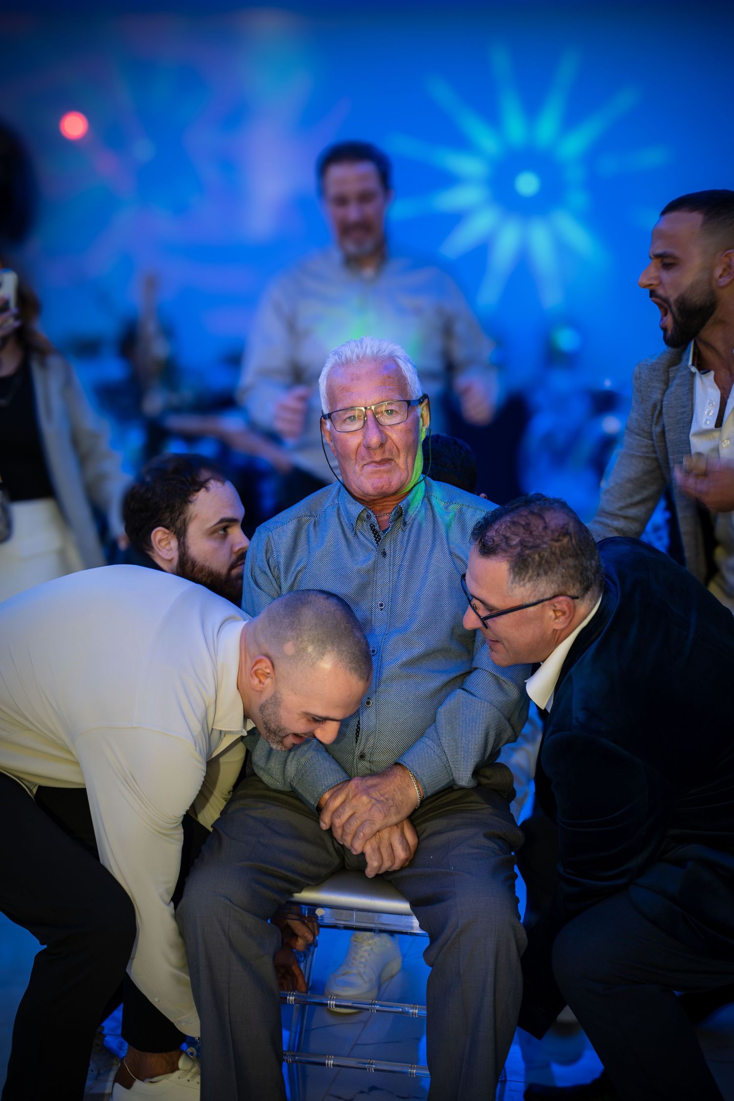 Intimate gathering around seated guest at party with blue lighting effects.