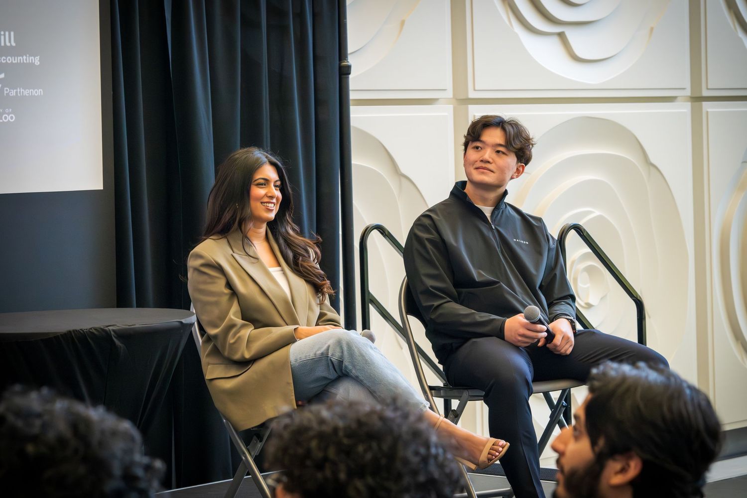 Speakers engaged in conversation during panel discussion on stage with decorative wall background.