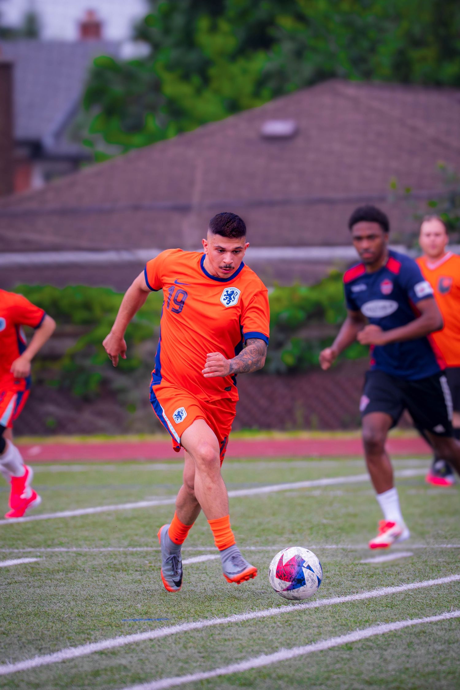 A player in orange controls the ball while dribbling across the soccer field.