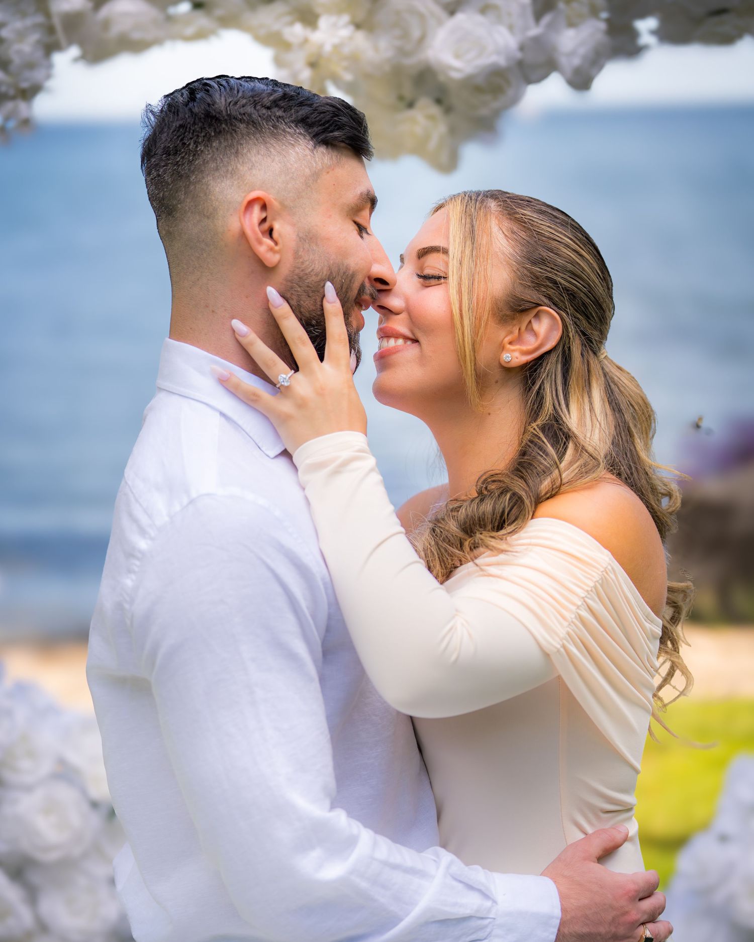 Tender moment between couple in white attire during golden hour.