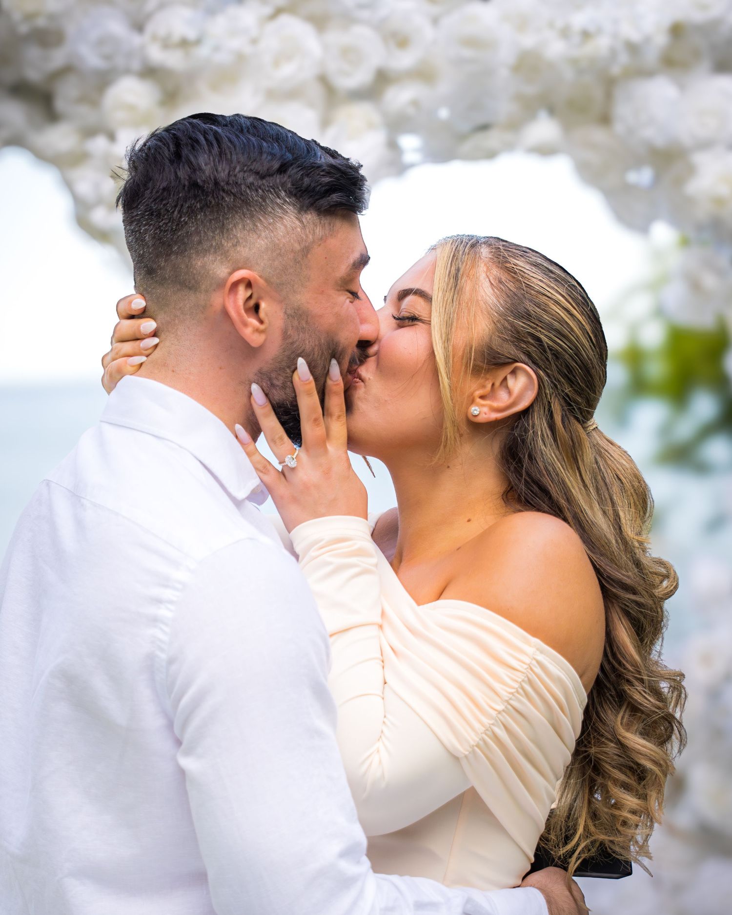 Romantic moment captured under white floral arch during sunset proposal.