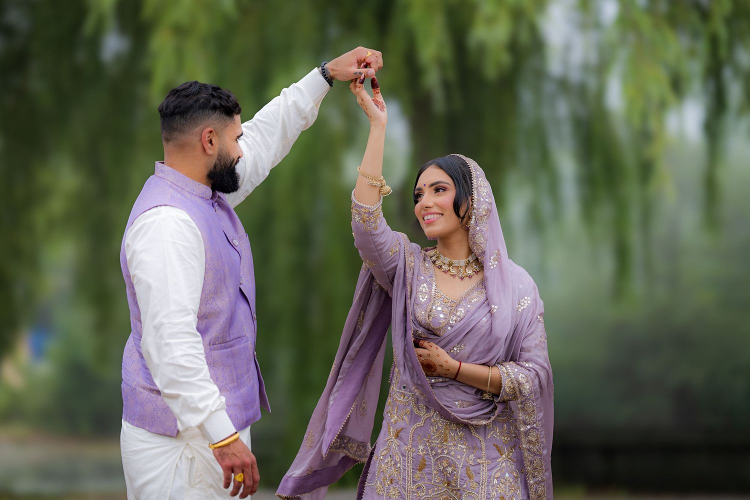 A couple in traditional South Asian attire dance and twirl together outdoors.