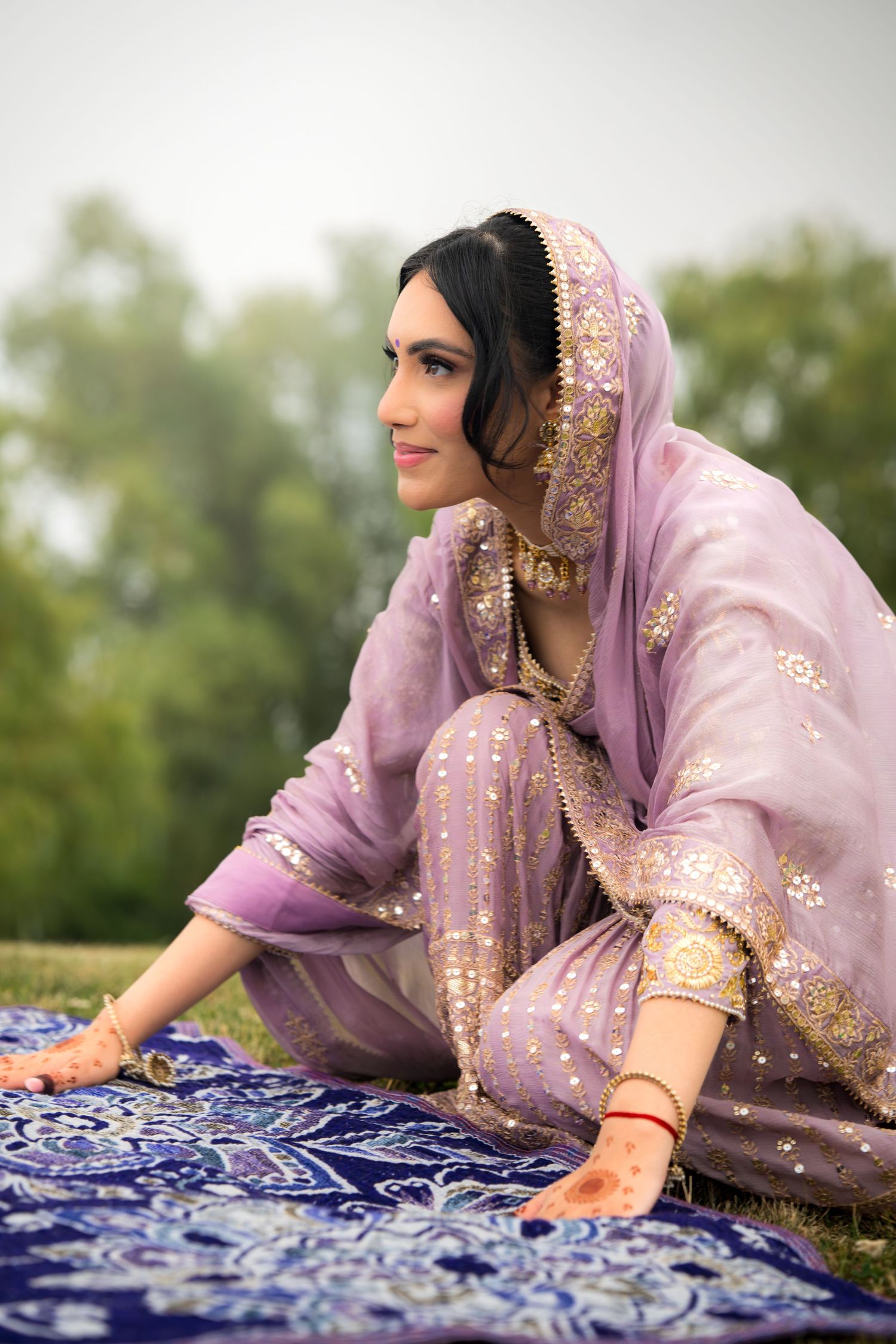 Person in lavender traditional attire examining detailed blue and white textile pattern on grass.