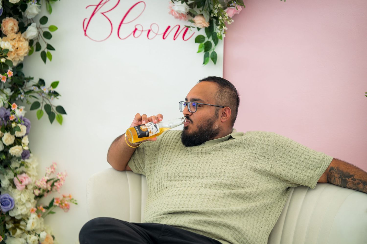 A person in a green shirt drinks from a glass against a floral wall backdrop.