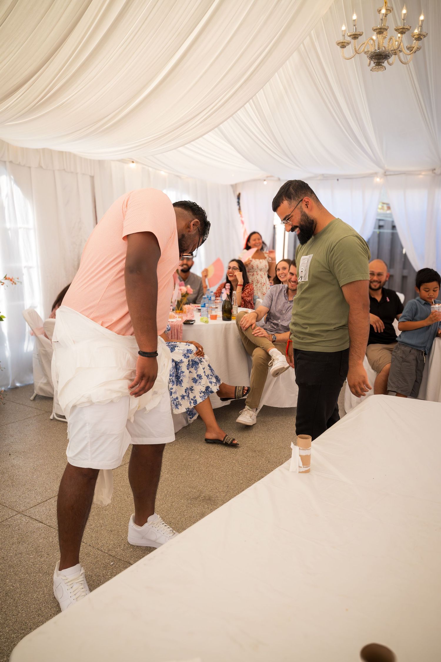 Wedding reception guests participating in an activity under elegant white tent draping.