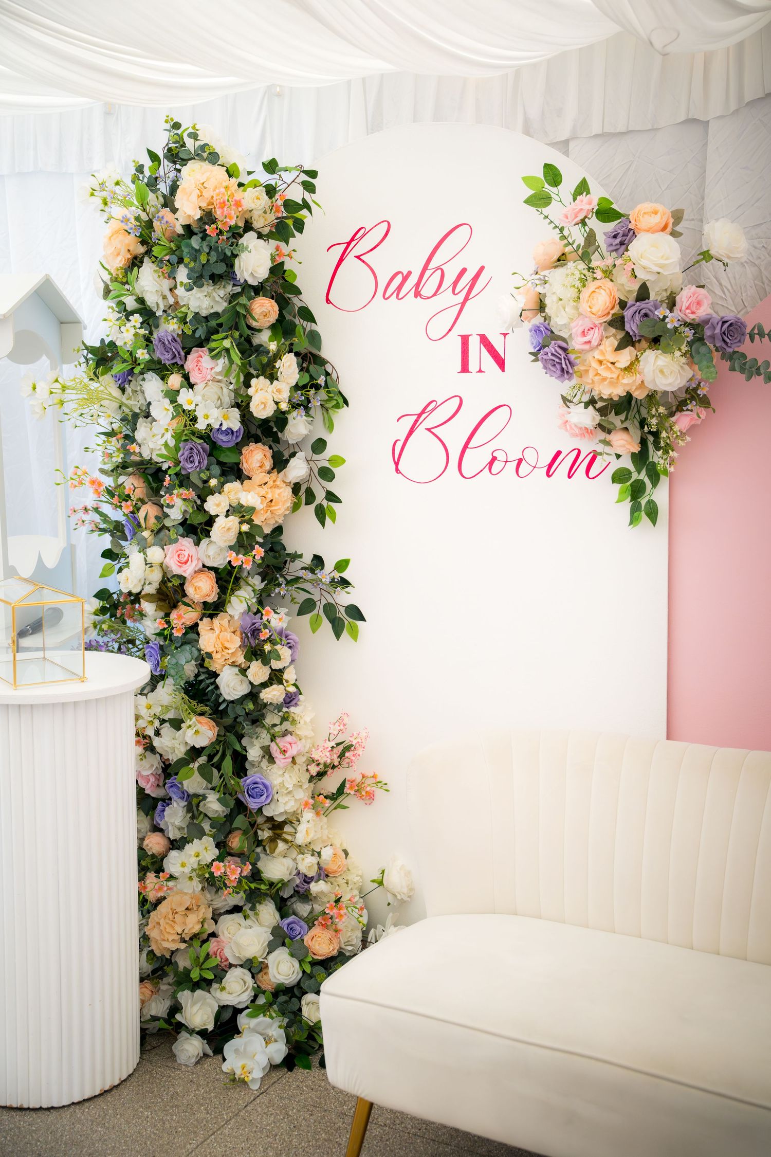 Elegant floral backdrop with pink and white roses against white paneling and pink accent wall for a baby shower.