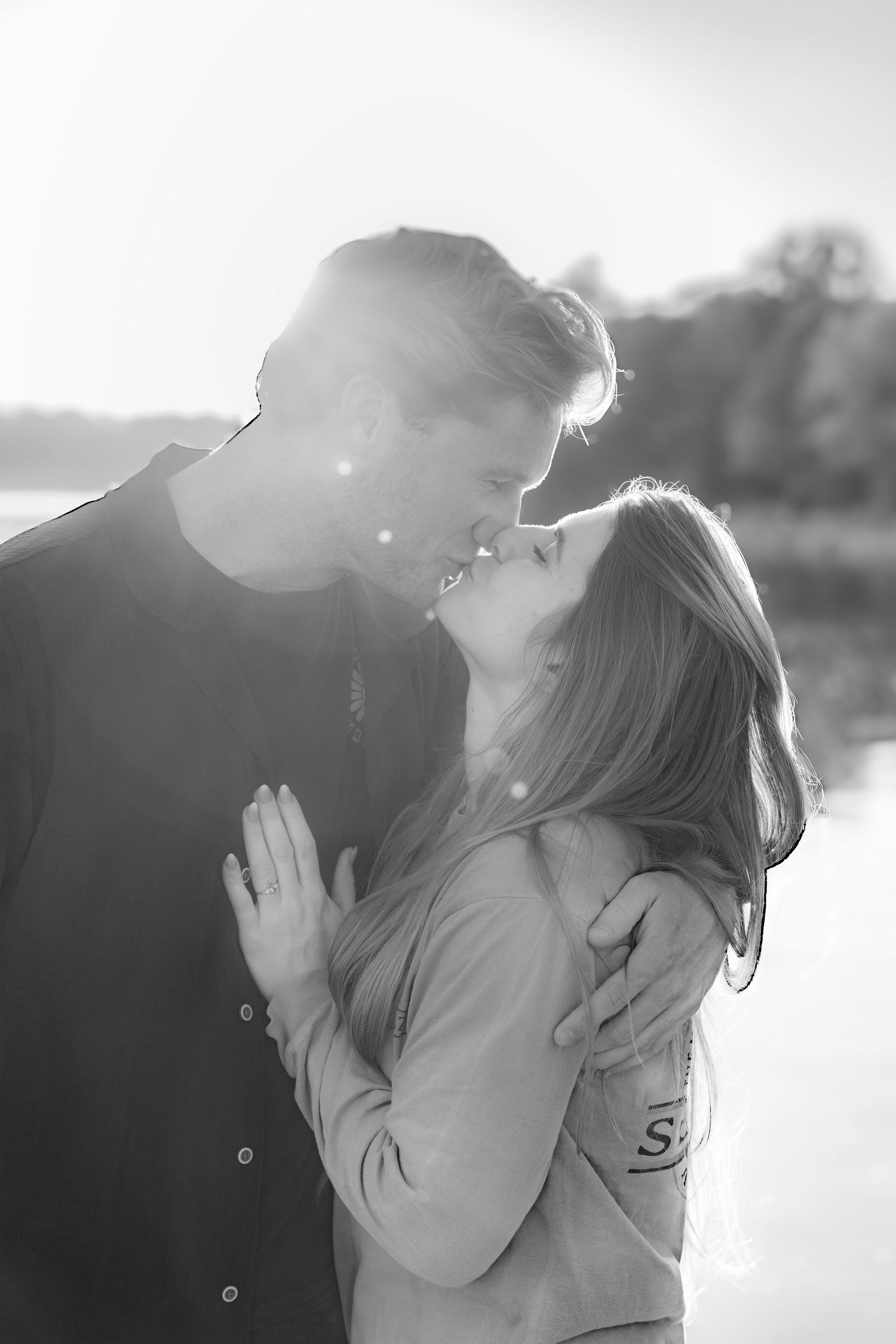 Black and white romantic photo of a couple about to kiss outdoors with sunlight glowing behind them.