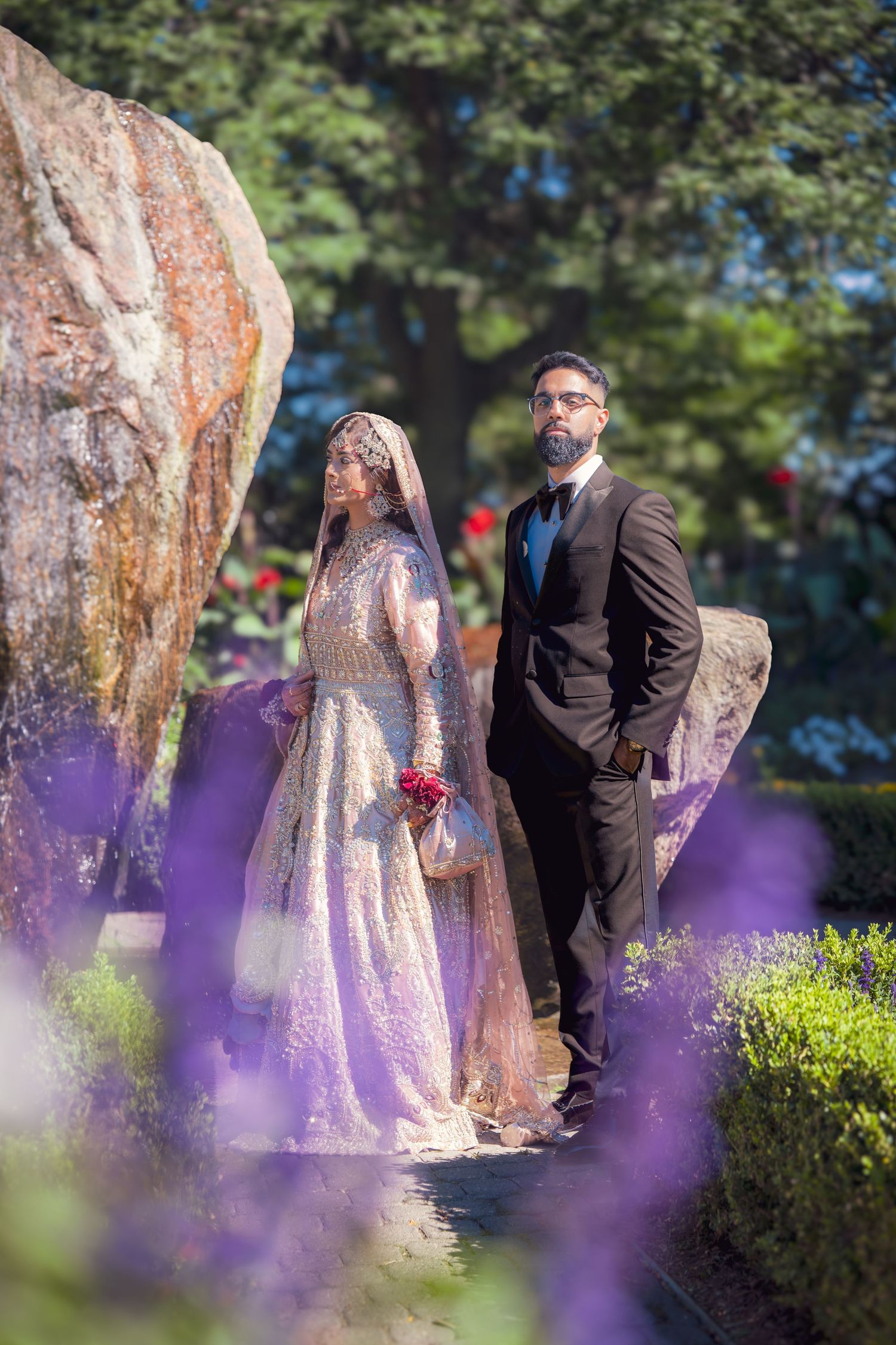 Wedding couple poses in garden with purple flowers in foreground creating dreamy effect.
