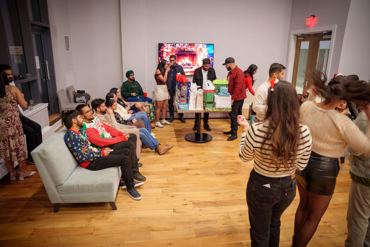 Wide shot of people gathered in a room with wooden floors and white walls.
