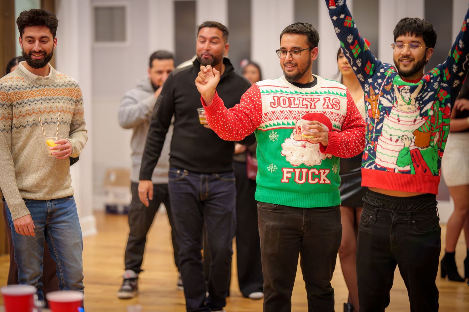 Party guests in holiday sweaters playing games at an indoor celebration.