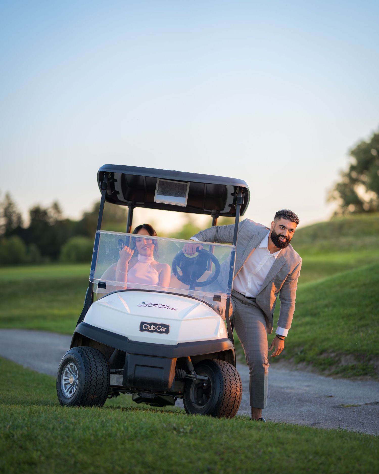 A golf cart sits on a path during sunset at a golf course.
