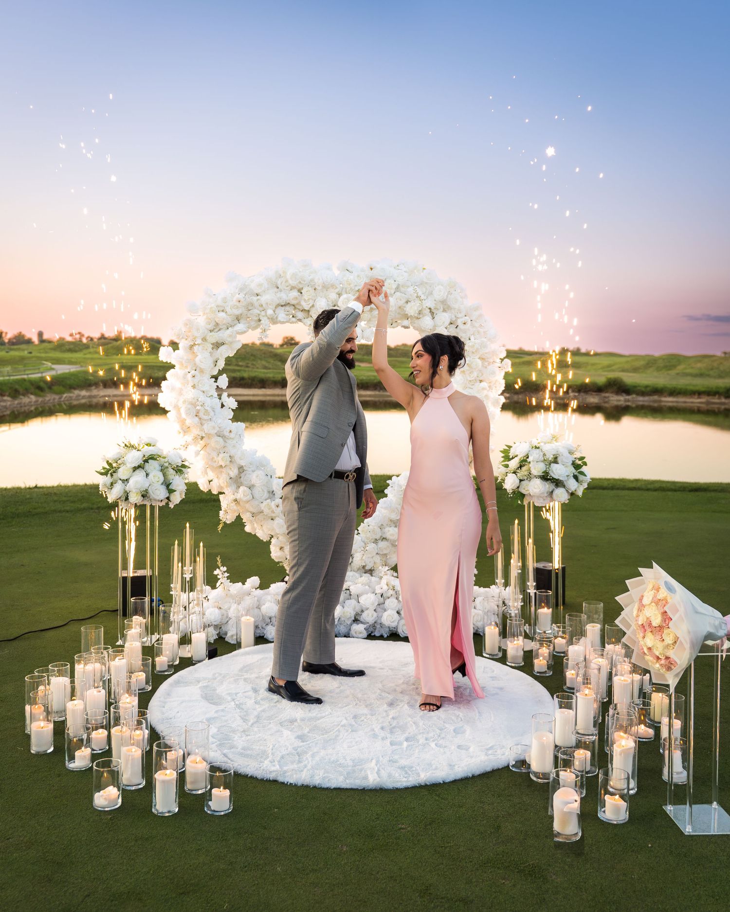 Romantic sunset proposal scene with white orchid arch and glowing candles on golf course.