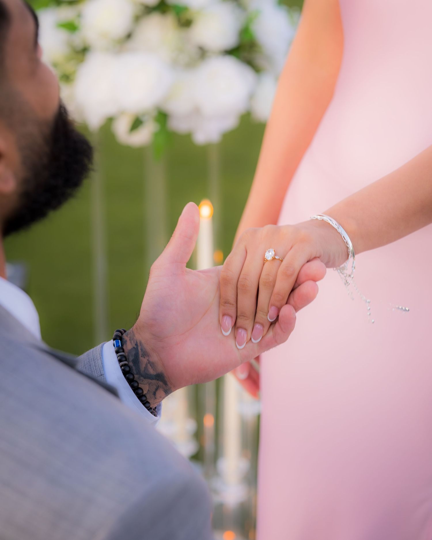 Detail shot of hands displaying an engagement ring with a pink dress in the background.