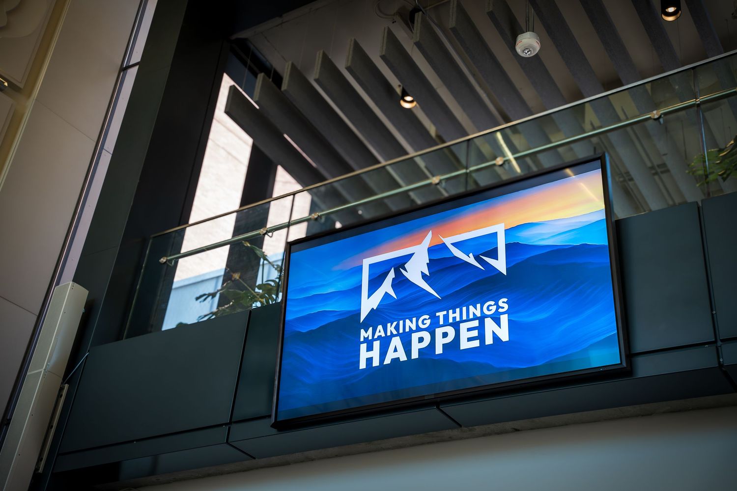 Blue illuminated signage mounted on a dark ceiling with industrial-style exposed ductwork and lighting fixtures.