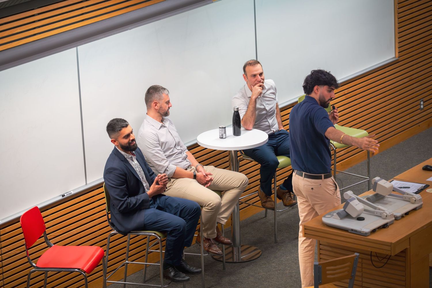 Casual office meeting with multiple attendees in a wood-paneled conference room.