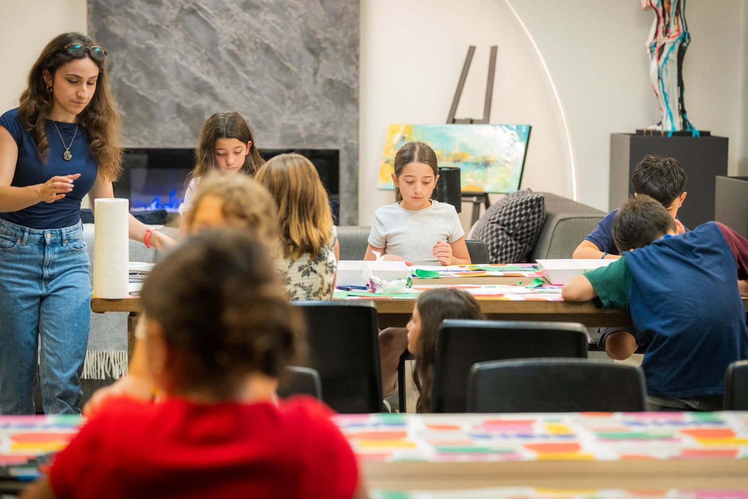 Students engage in an art workshop, drawing and painting at tables in a modern gallery studio space.