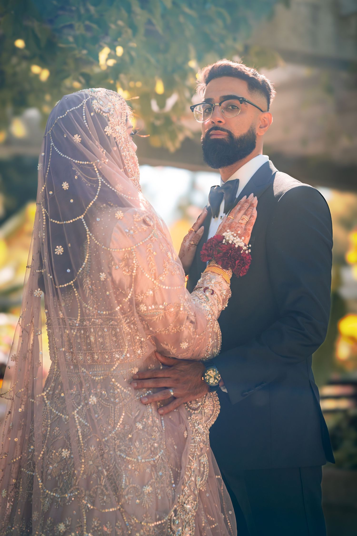 Romantic wedding couple poses in outdoor setting with golden sunlight filtering through trees.