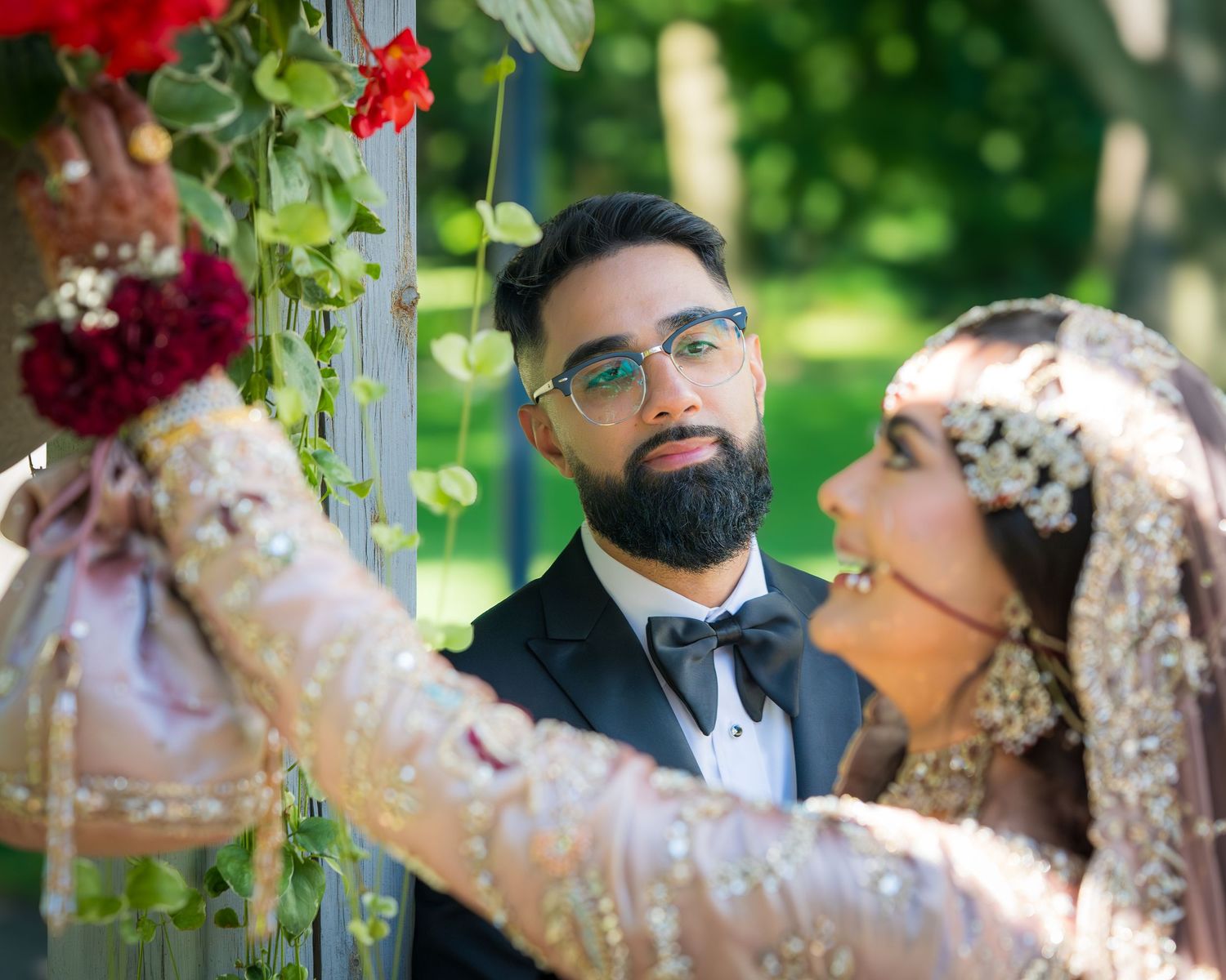Wedding couple sharing an intimate moment in a garden with red flowers and hanging decorations.
