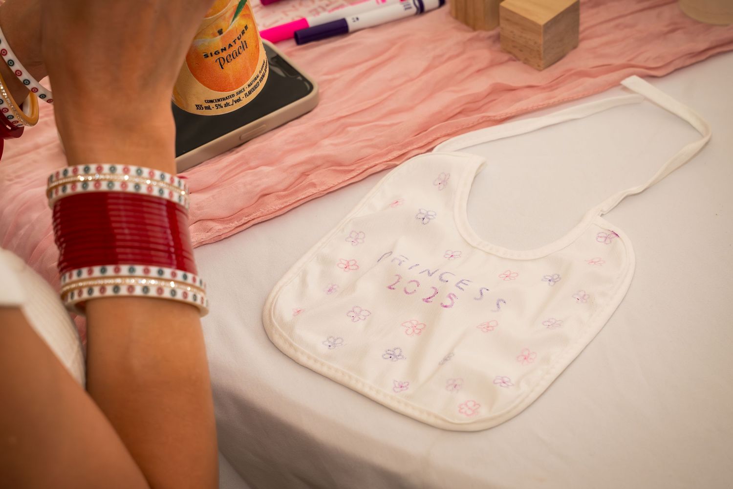 Detailed view of decorated baby bib with bangles visible in foreground.