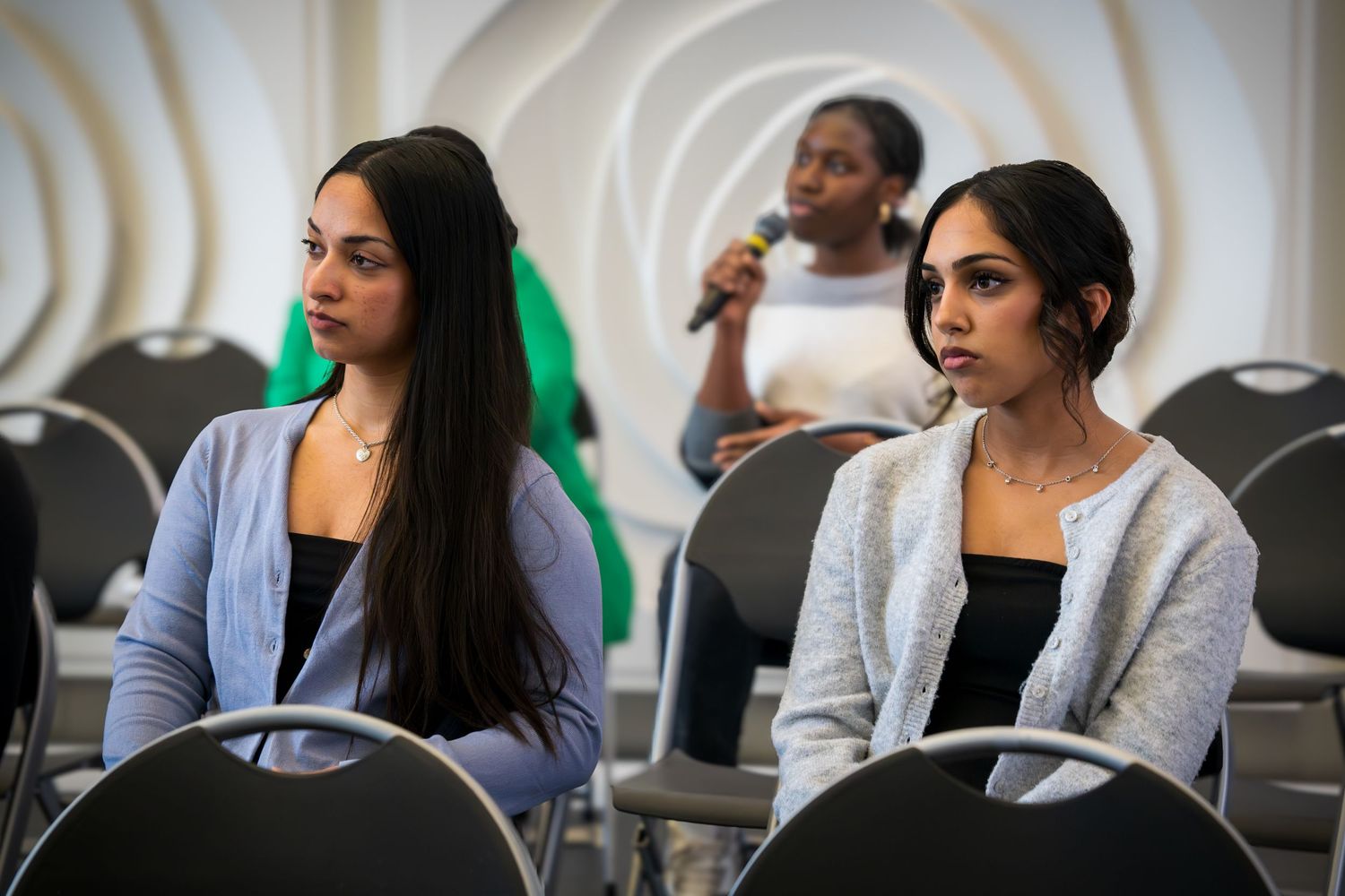 Professional speakers engage in conversation during a panel event with geometric wall decor.
