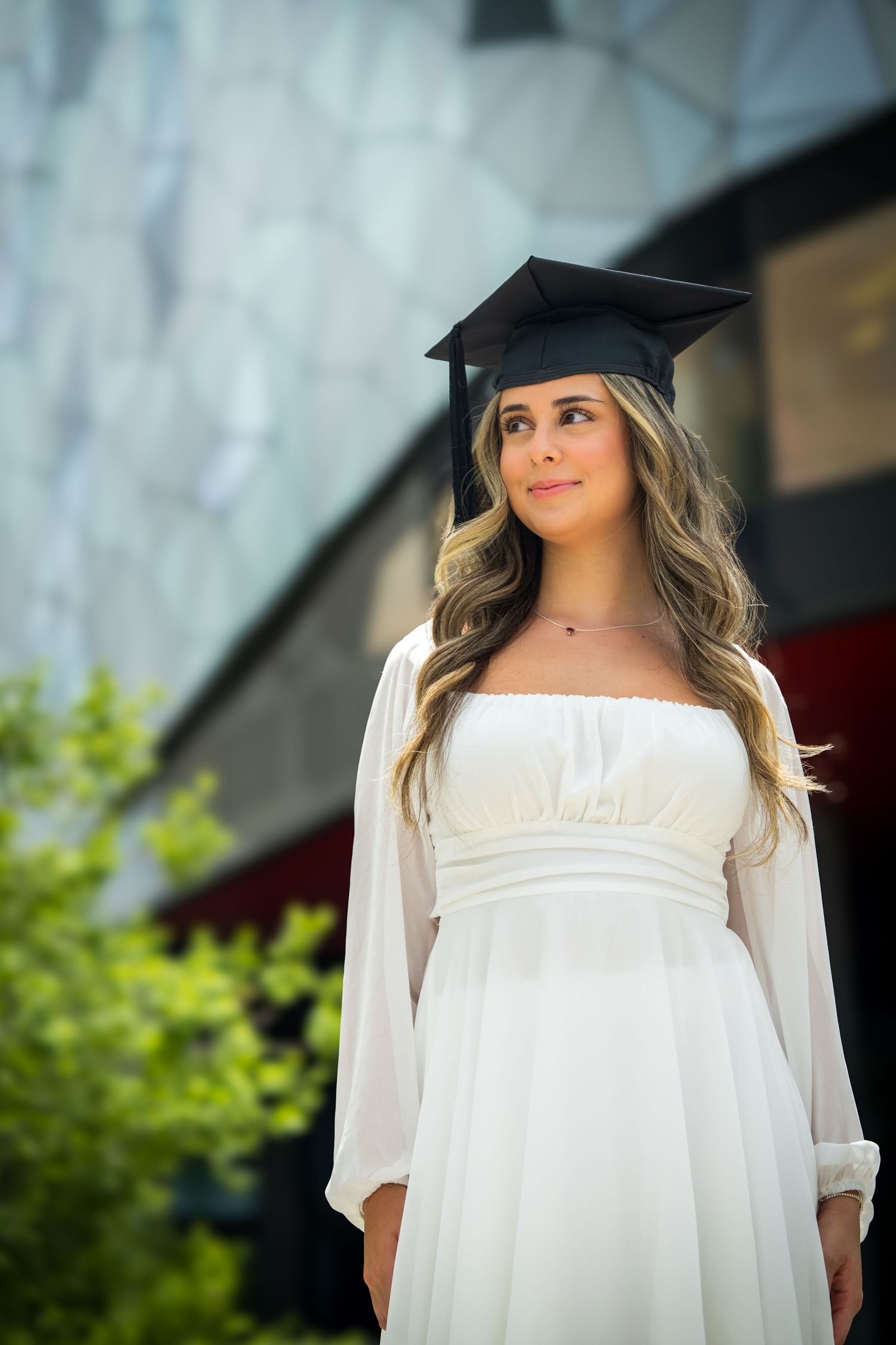 Graduation portrait featuring white dress and black cap against architectural background.