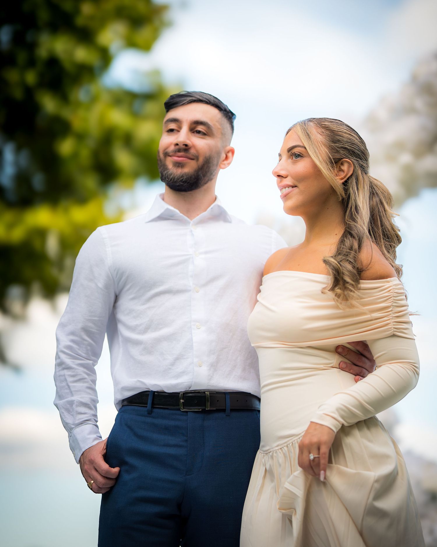 Couple in formal attire stands together outdoors during a special occasion.