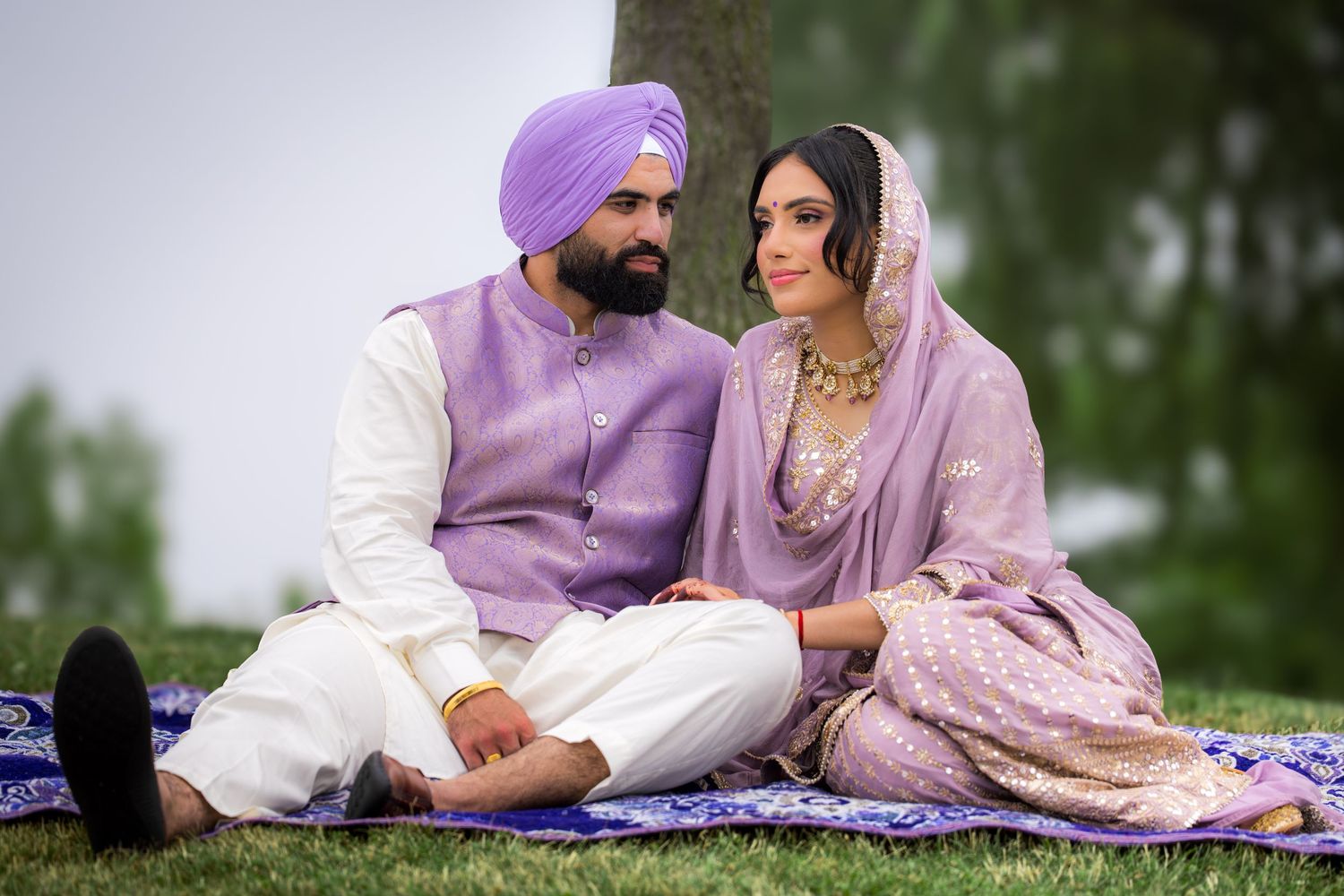 A group poses casually on a blue blanket outdoors wearing coordinated traditional Indian-inspired clothing.