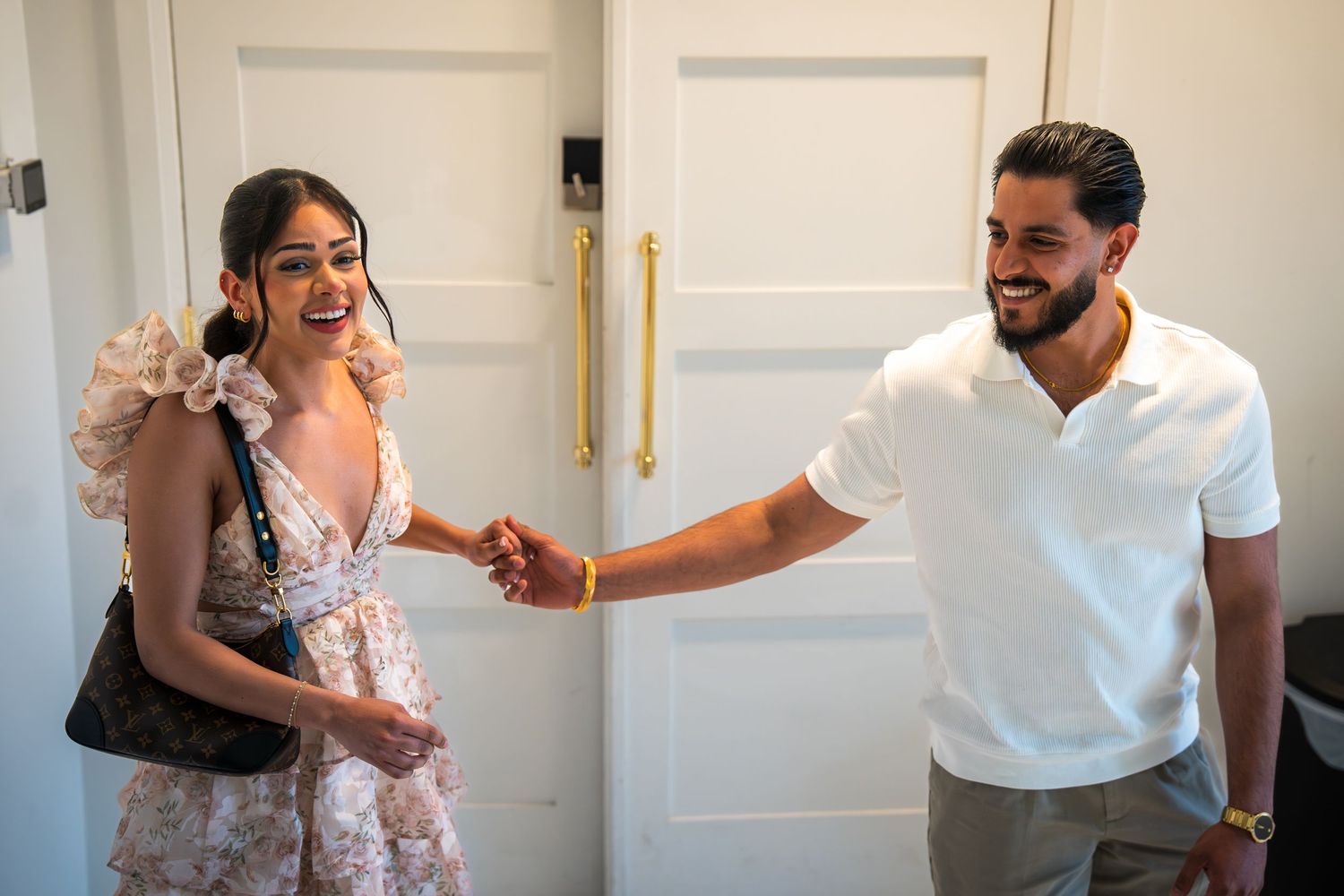 A man and woman shake hands and smile warmly while standing in front of elegant white double doors.