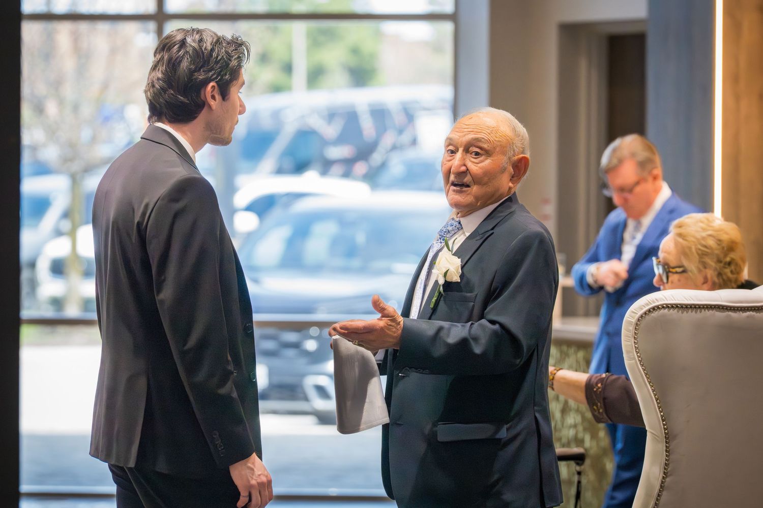 Two men in suits engaged in conversation near large windows at an elegant event venue reception area.