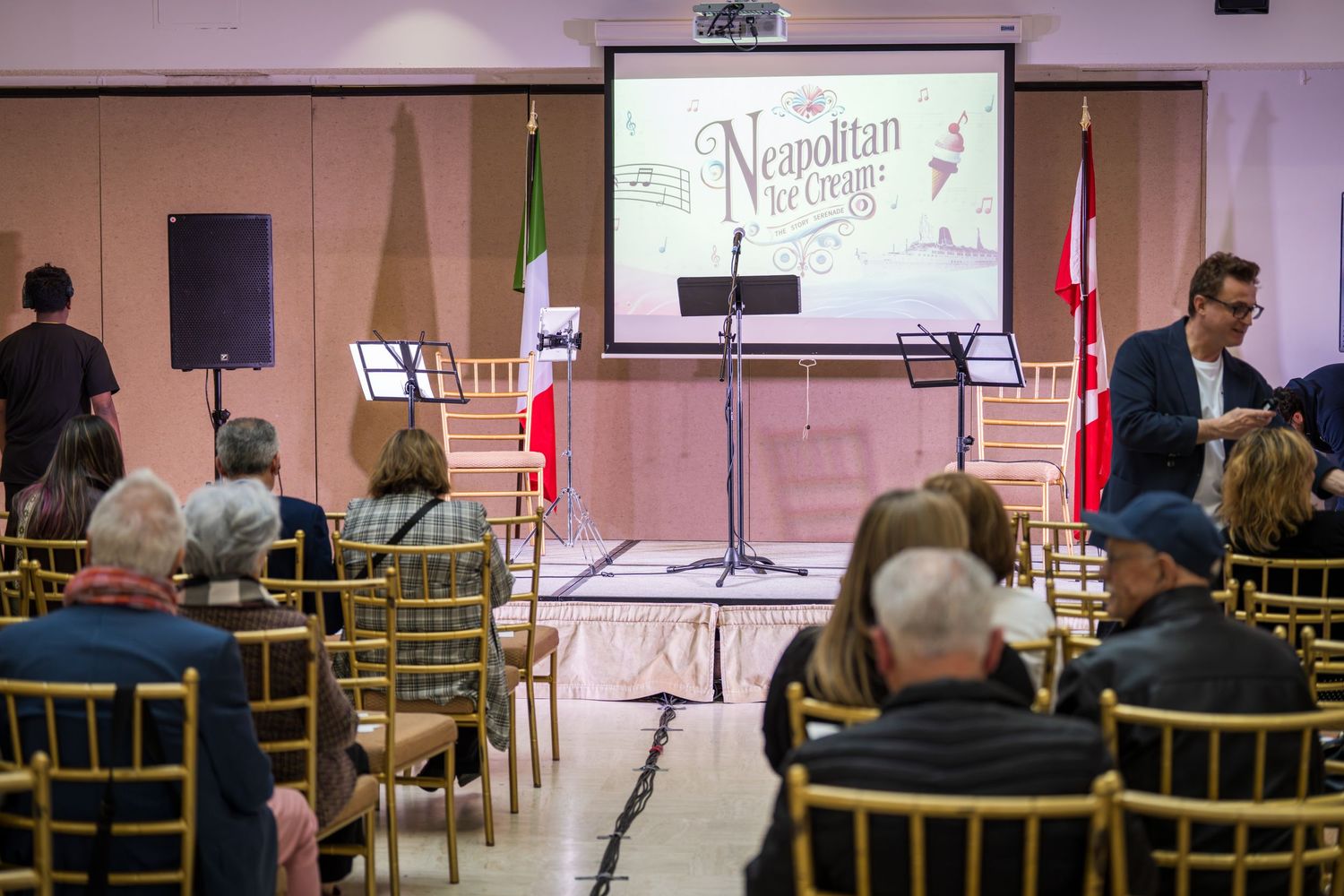 Audience seated in chairs at a Neapolitan Ice Cream event with a presentation screen and Italian and Canadian flags.