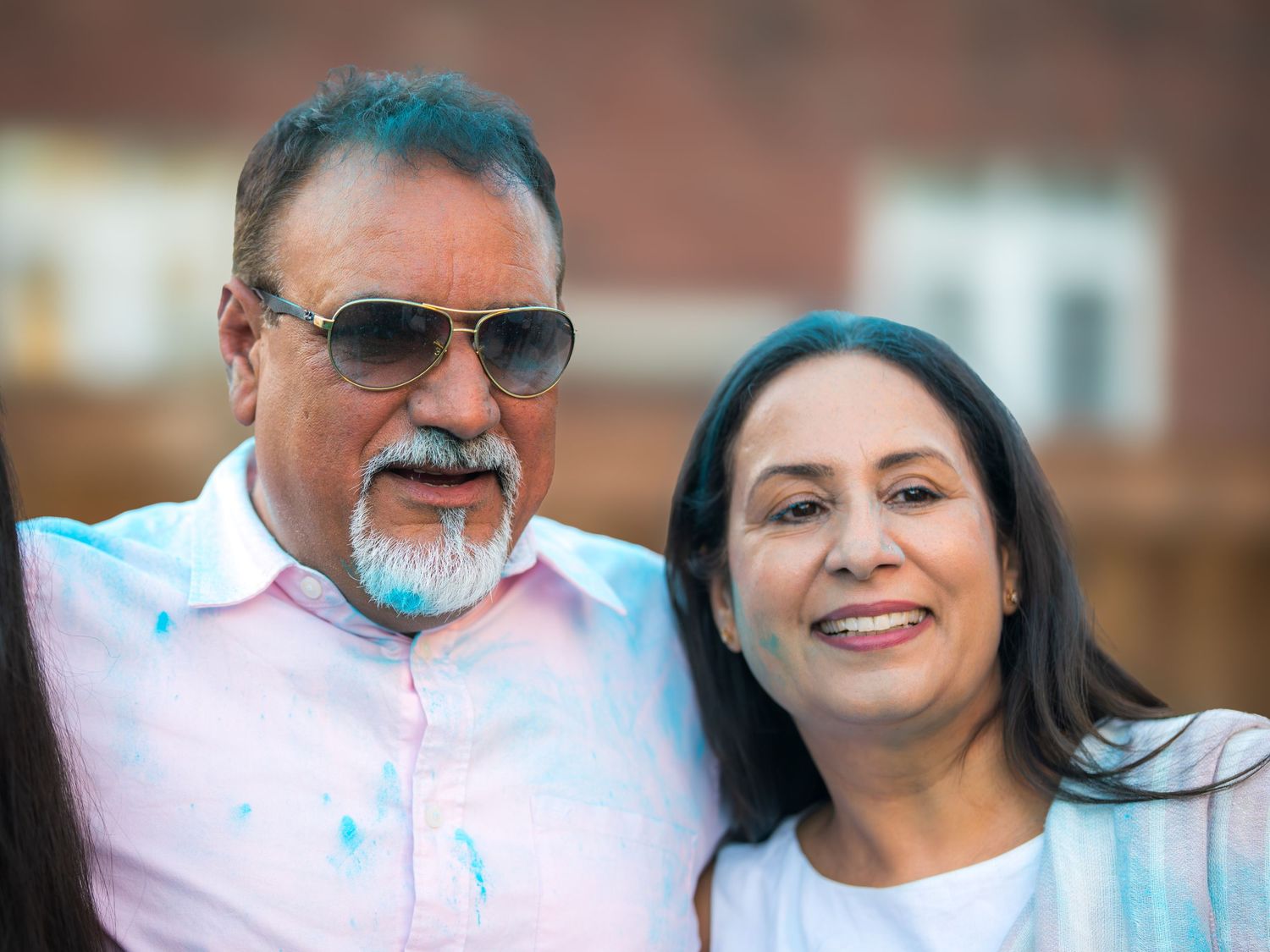 Smiling couple with blue gender reveal powder on their clothes posing together outdoors at a gender reveal party.