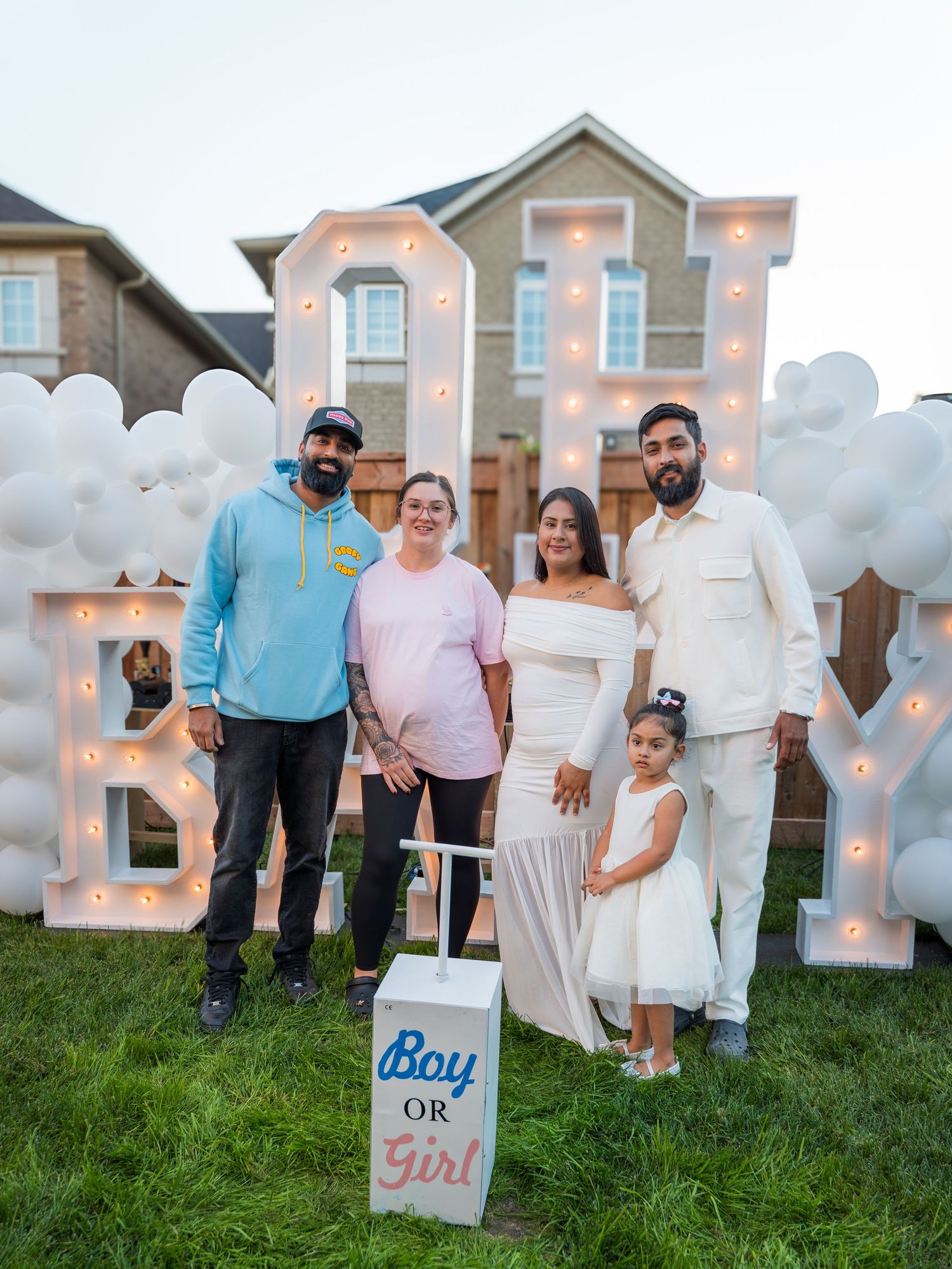 Group of five pose at a Boy or Girl gender reveal party with illuminated BABY marquee letters outdoors.