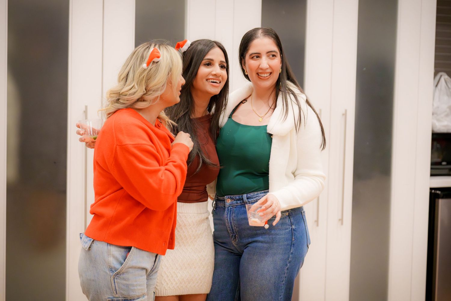 Three friends in casual outfits chatting during an indoor social gathering.