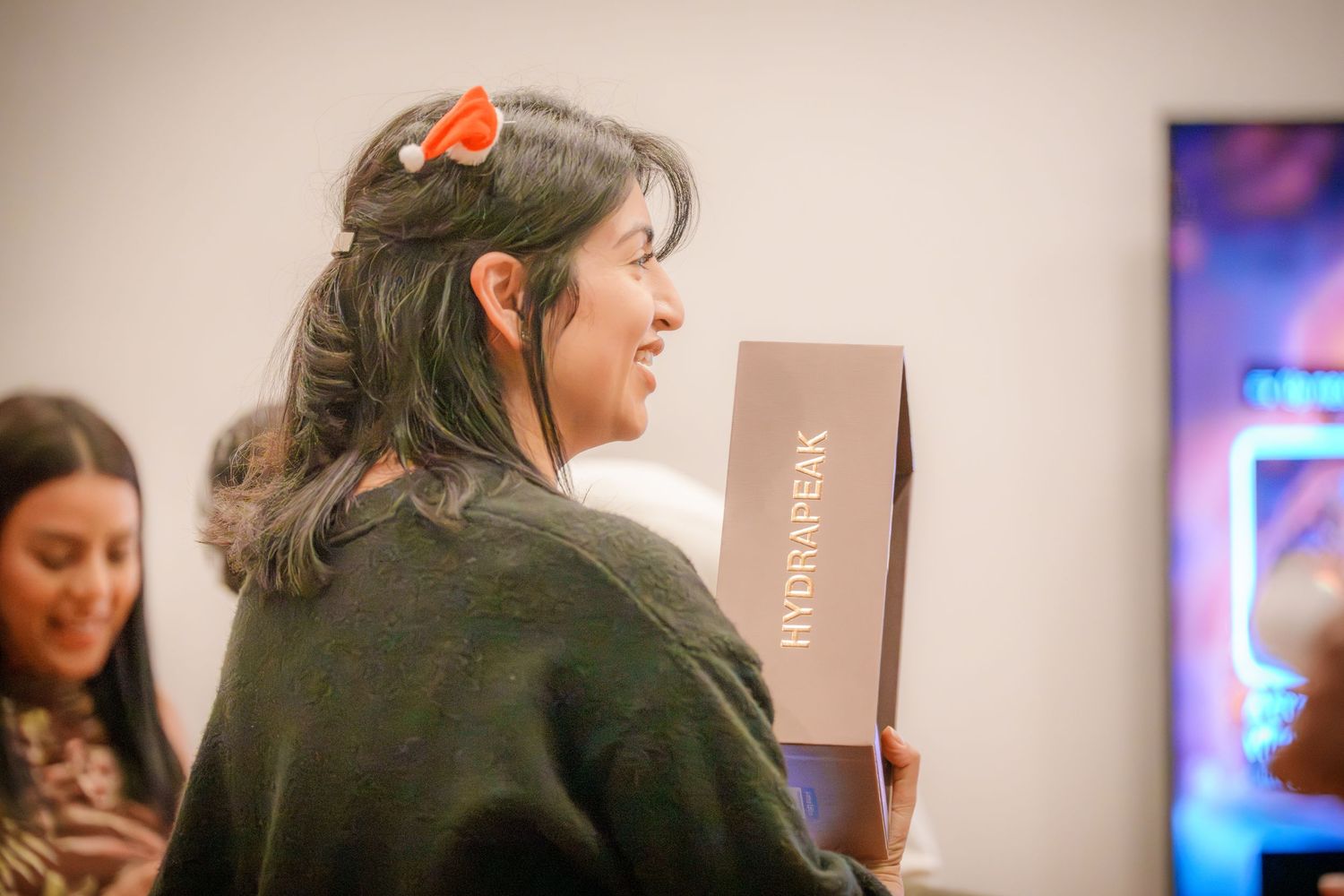 A guest in casual attire holds a gift box at a holiday party.