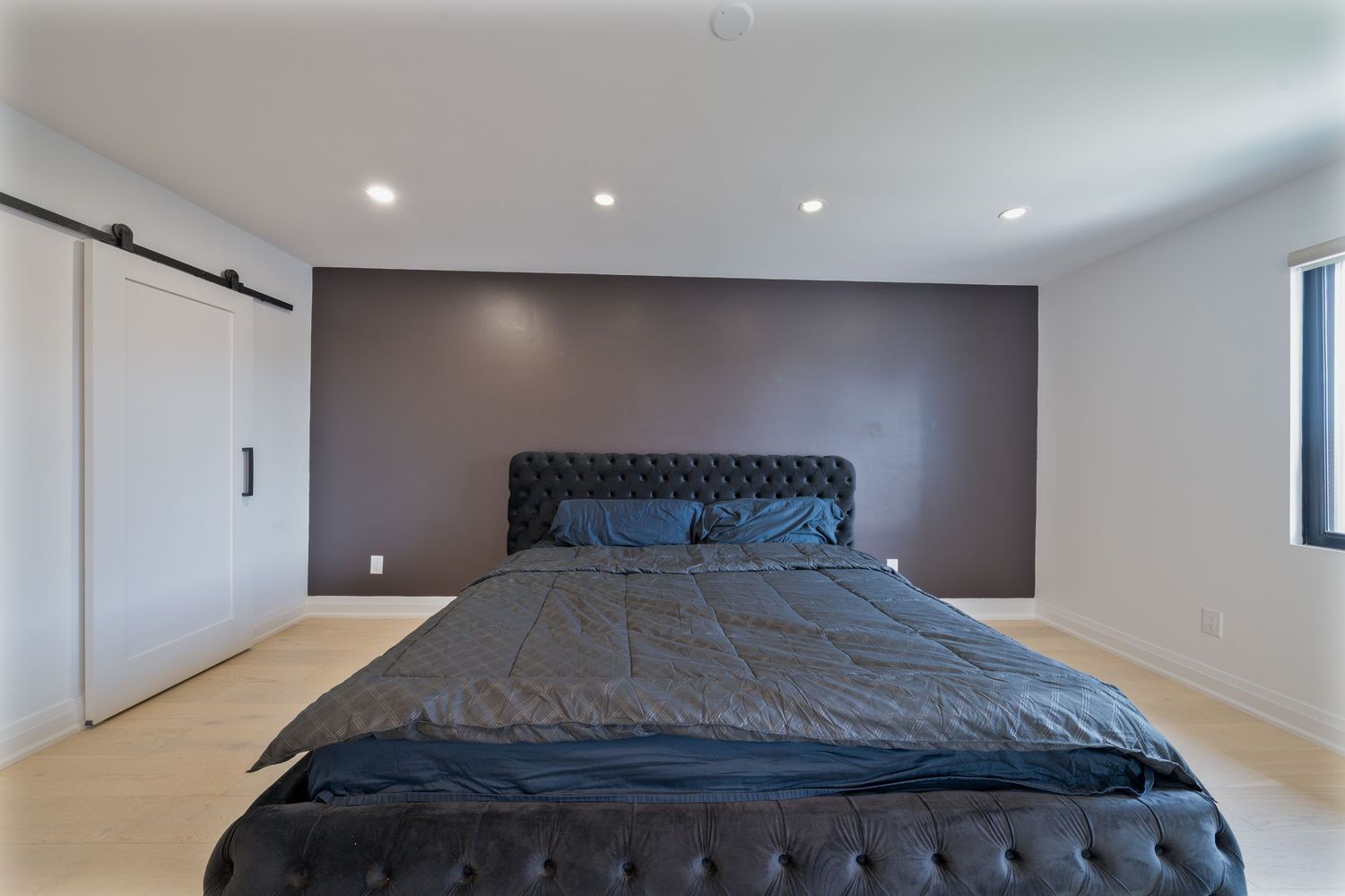 Modern bedroom interior with gray bedding and recessed lighting in a minimalist white and gray color scheme.