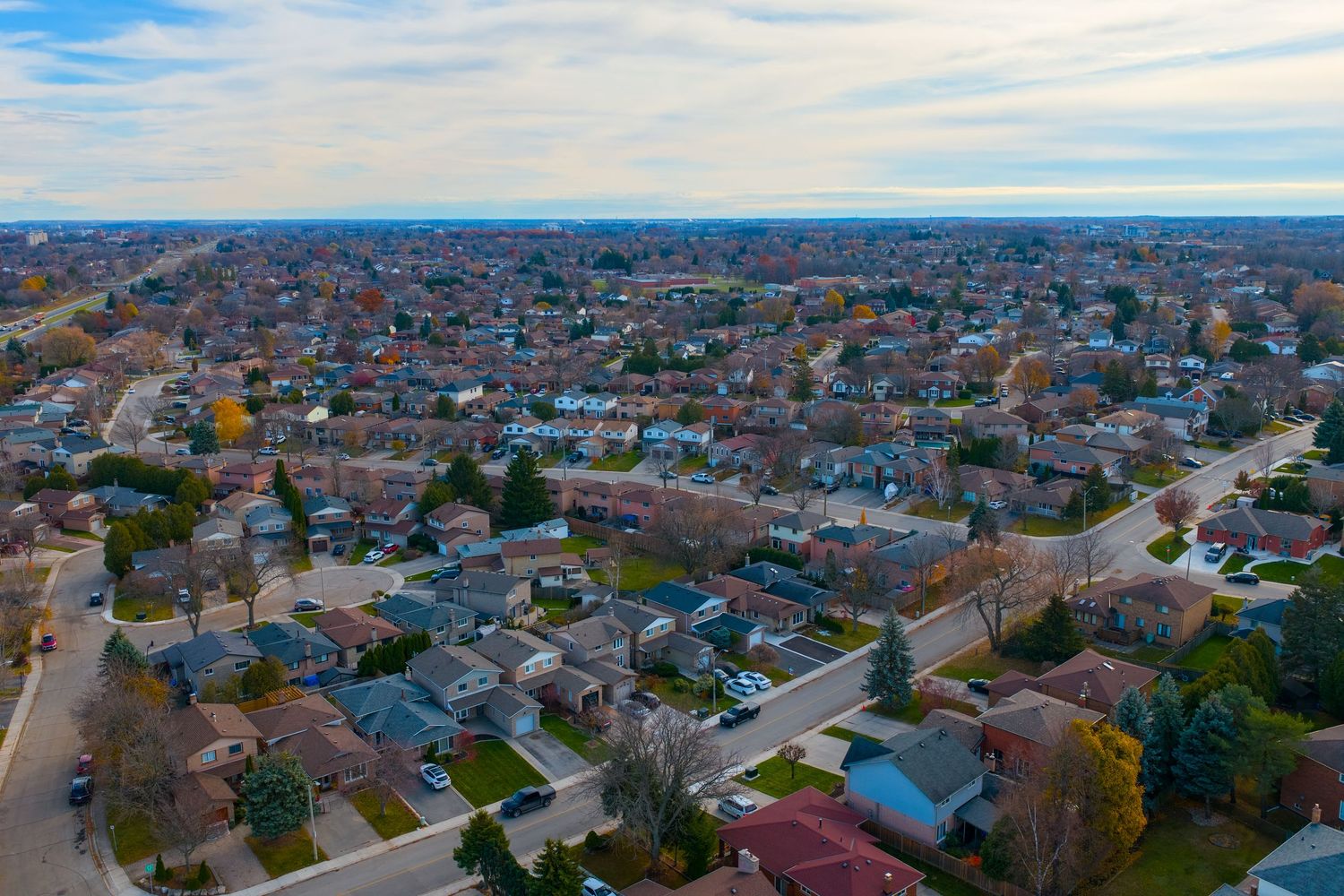 Aerial panoramic view of residential neighborhoods with houses and trees stretching to the horizon under blue sky.