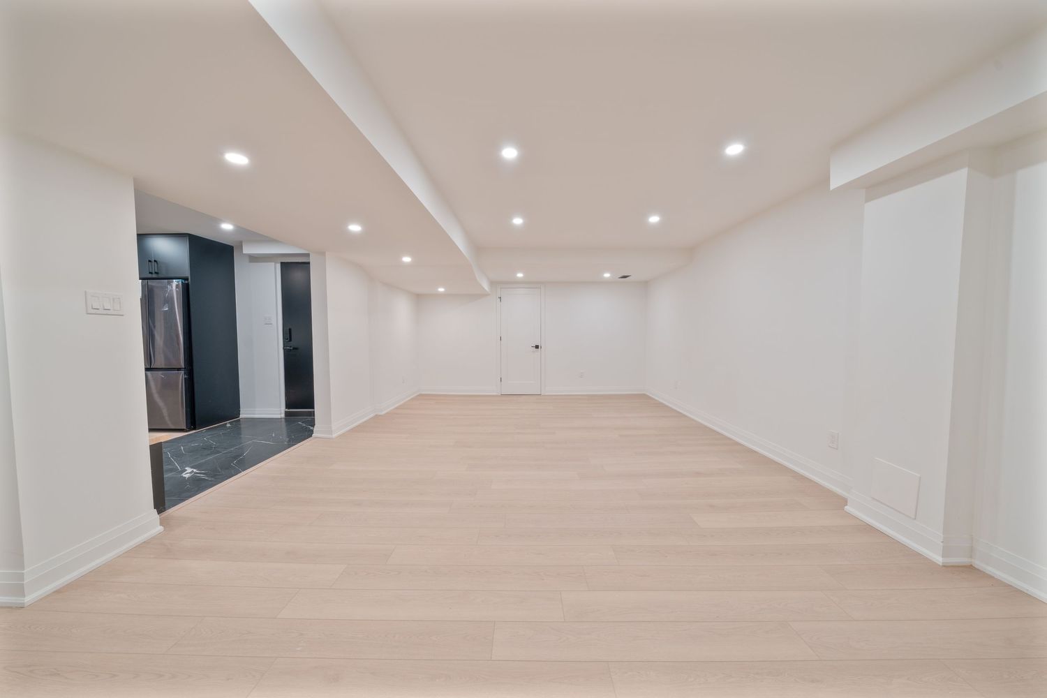 Modern office hallway with white walls, recessed lighting and light wood flooring extending into the distance.