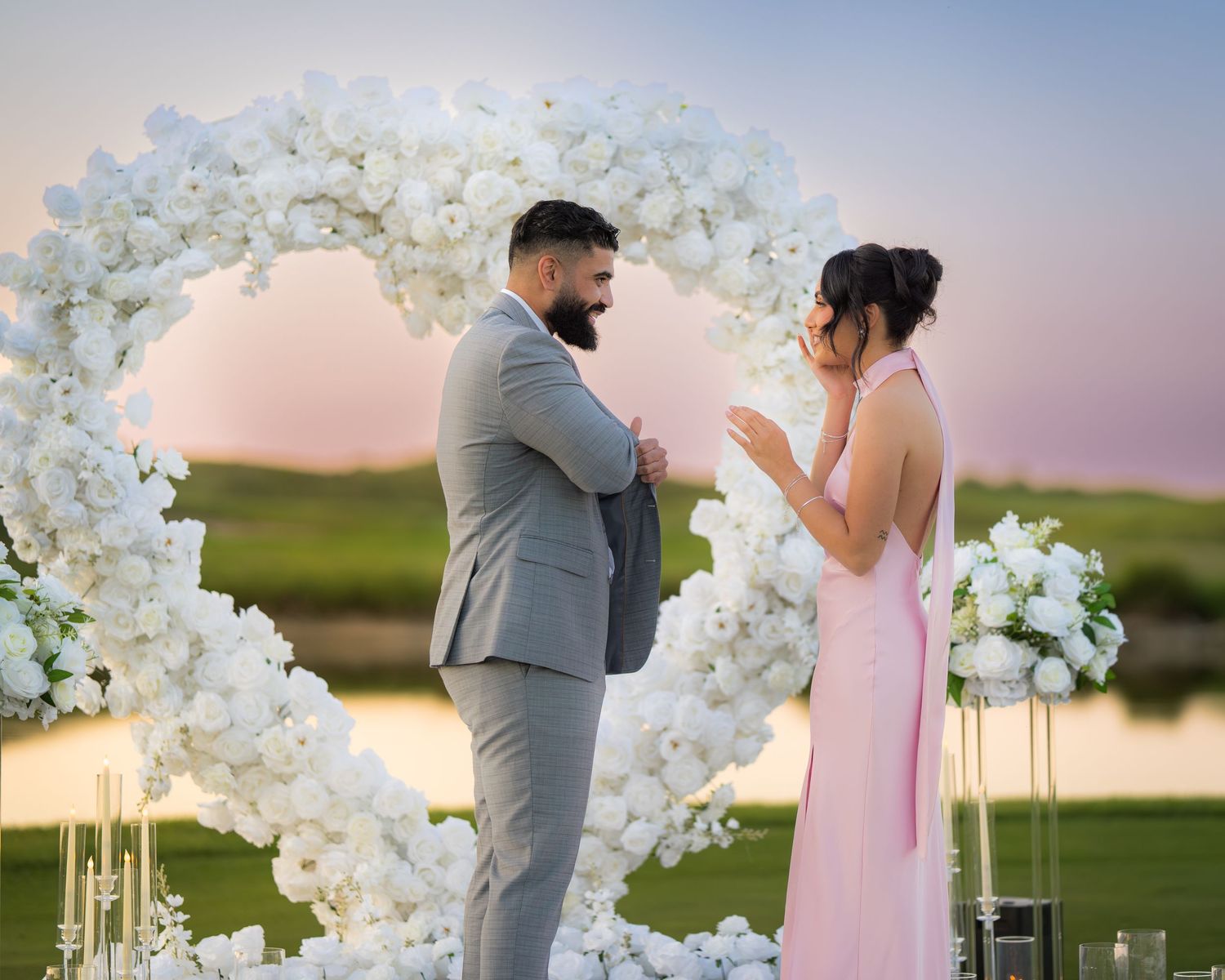 Beautiful proposal setting with white floral archway and candlelit path during golden hour.