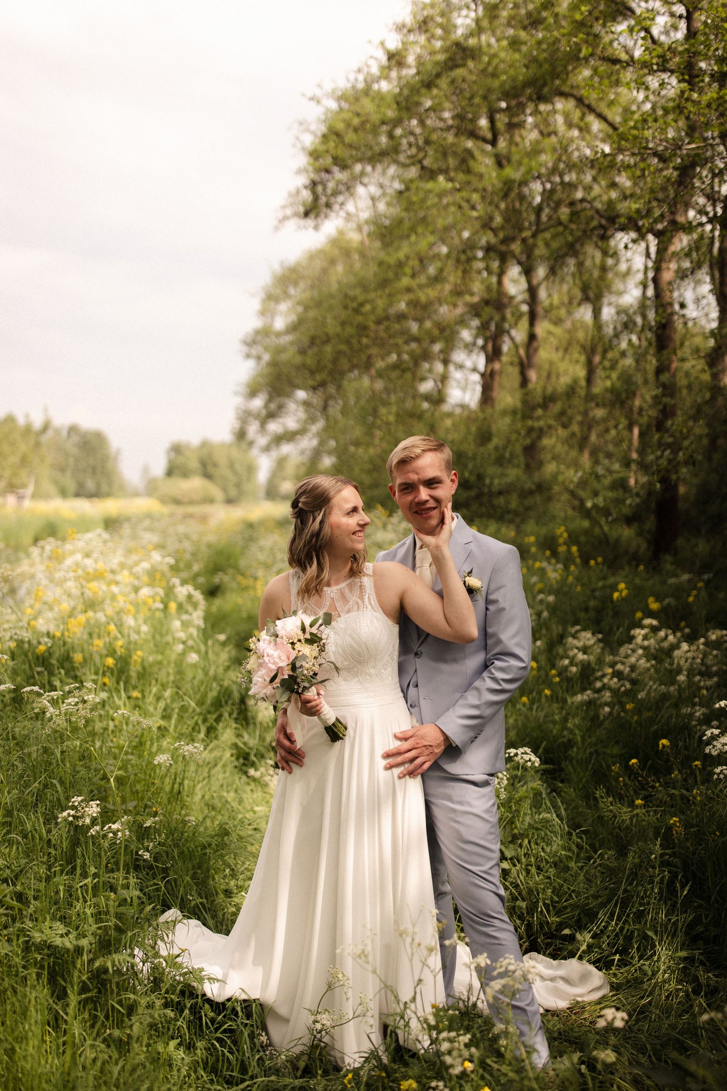 A newlywed couple shares an intimate moment while standing in a green meadow filled with wildflowers.