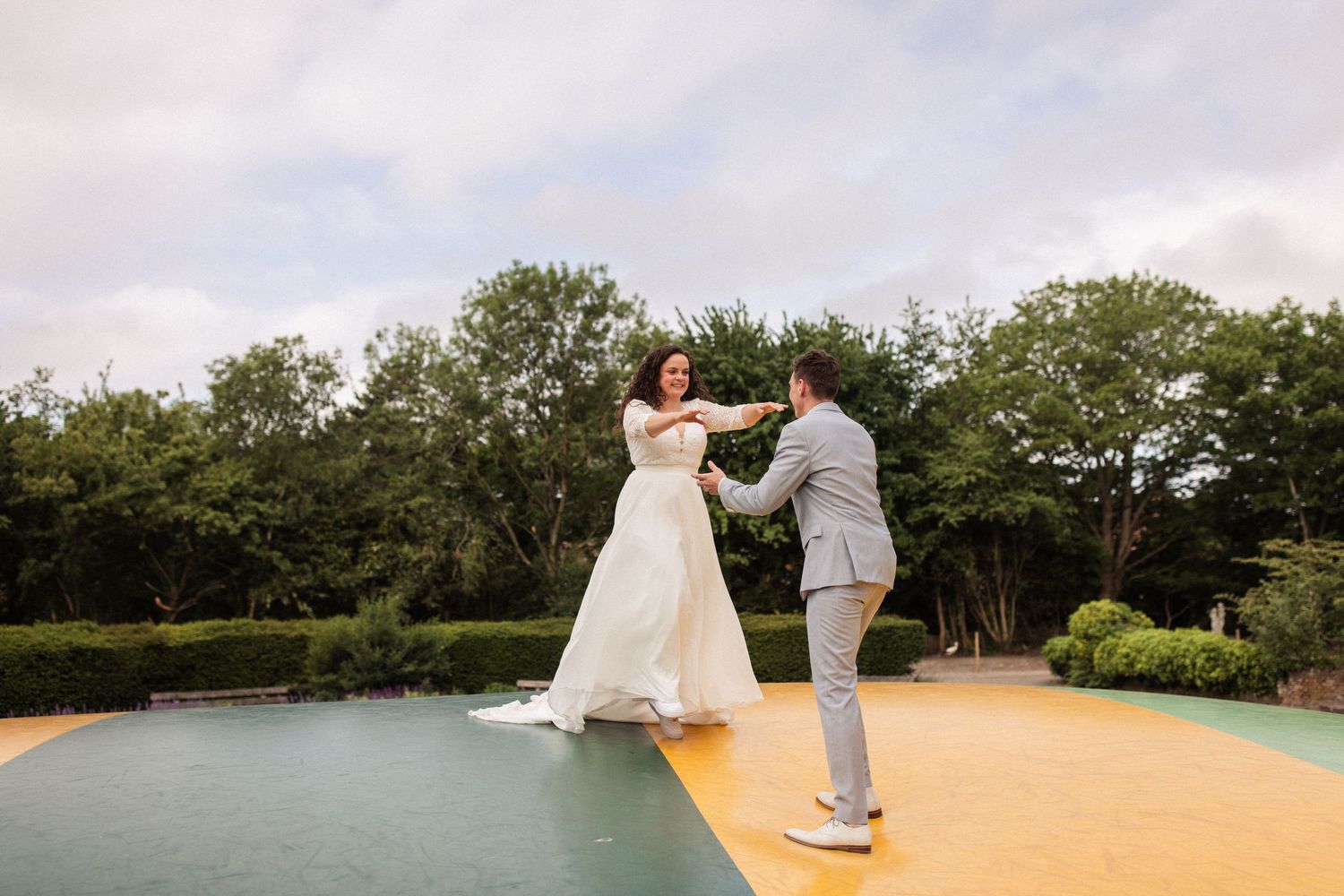 A couple dances playfully on a yellow platform surrounded by garden scenery.